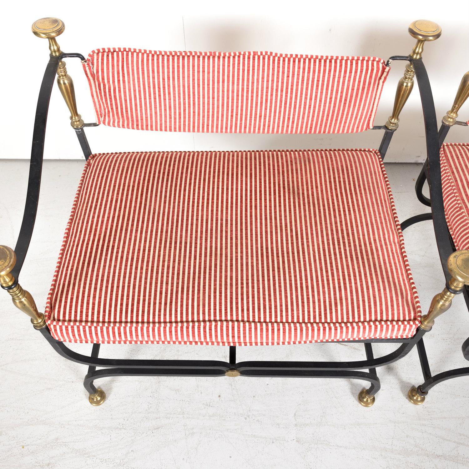 A handsome pair of Italian Savonarola chairs or benches having sculptural black wrought iron frames with turned brass uprights topped with large brass pommels, X-stretchers decorated with brass floral medallions, and brass feet, circa 1950s. Striped