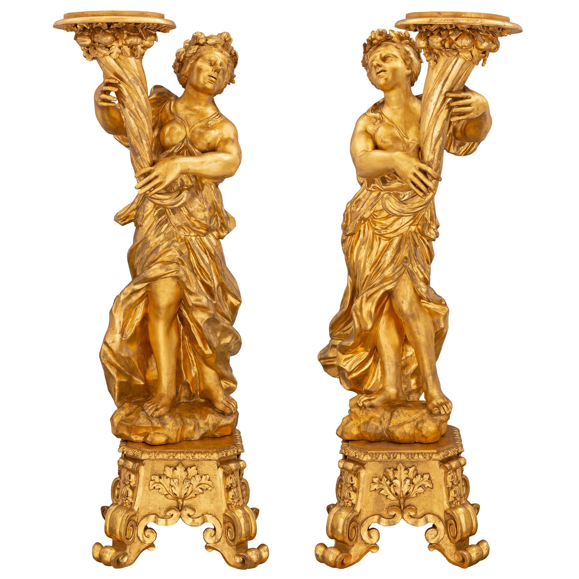 Une paire sensationnelle et monumentale de Torchières en bois doré de la période baroque de la fin du XVIIe siècle. Chaque torchère est surélevée par une base carrée effilée avec de remarquables pieds à volutes très décoratifs et d'élégantes
