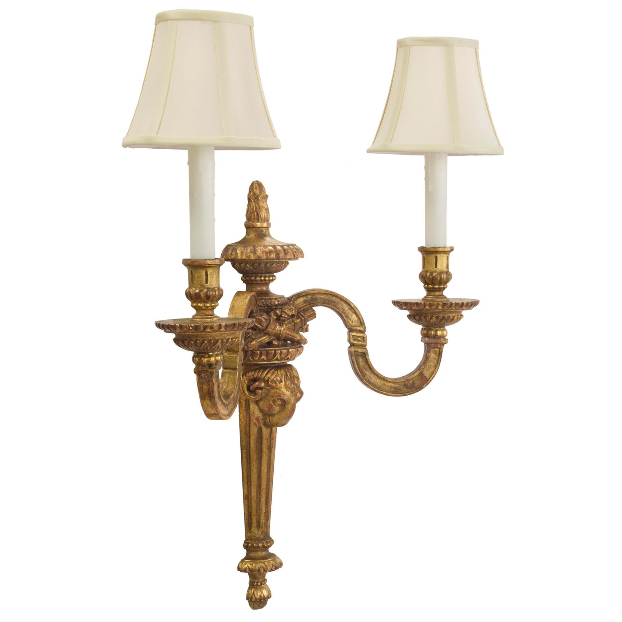 A very attractive pair of Italian late 19th century Louis XVI style giltwood sconces. Each sconce has a reeded tapered base with inverted finial topped by a ram head. The two S-scrolled electrified arms are centered by a carved quiver with arrows