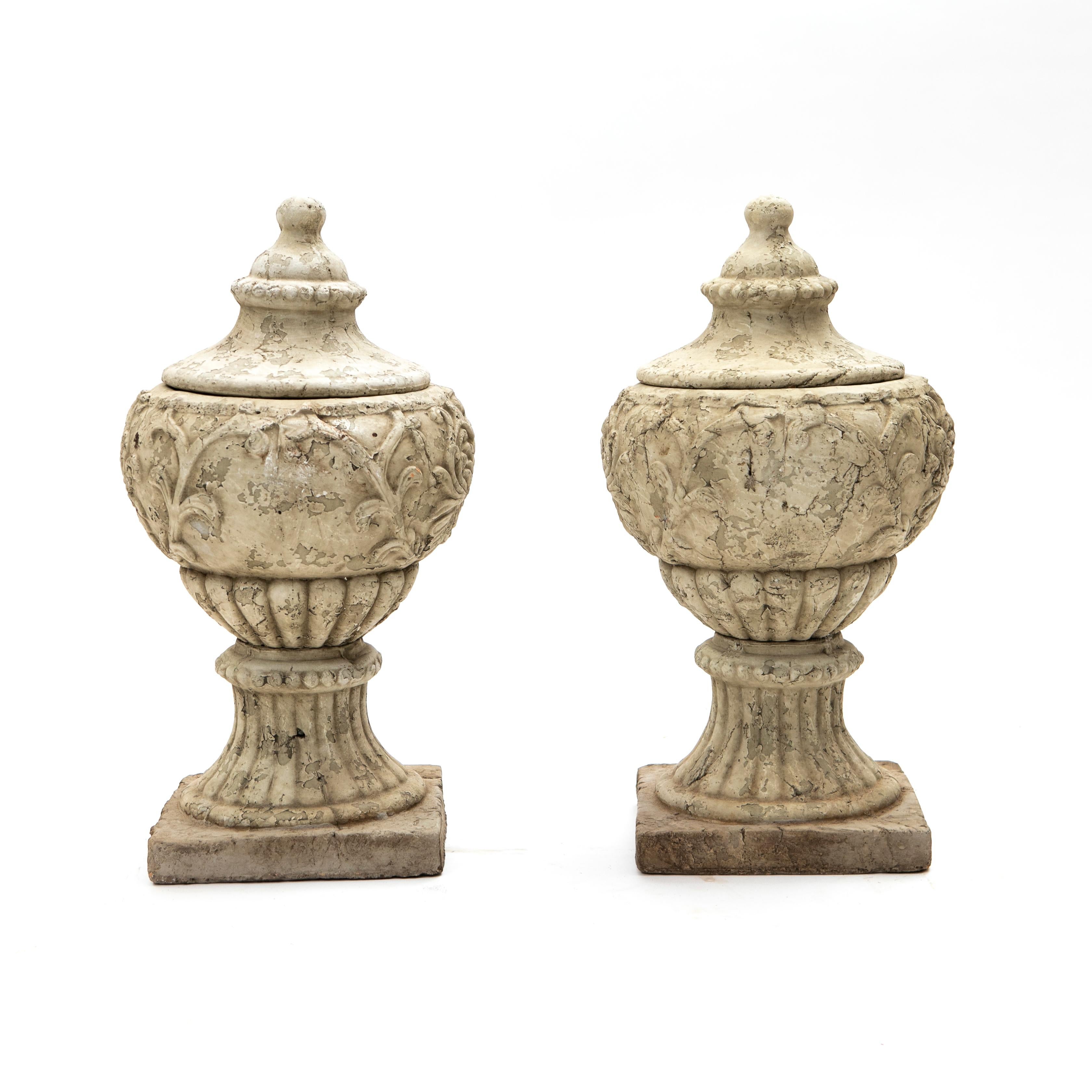 Pair of decorative Italian urns with lid made of grey painted terracotta with natural age-related patina.

Each with scrolling foliate relief and fluted decoration raised on pedestal bases.

Italy 1850-1870.