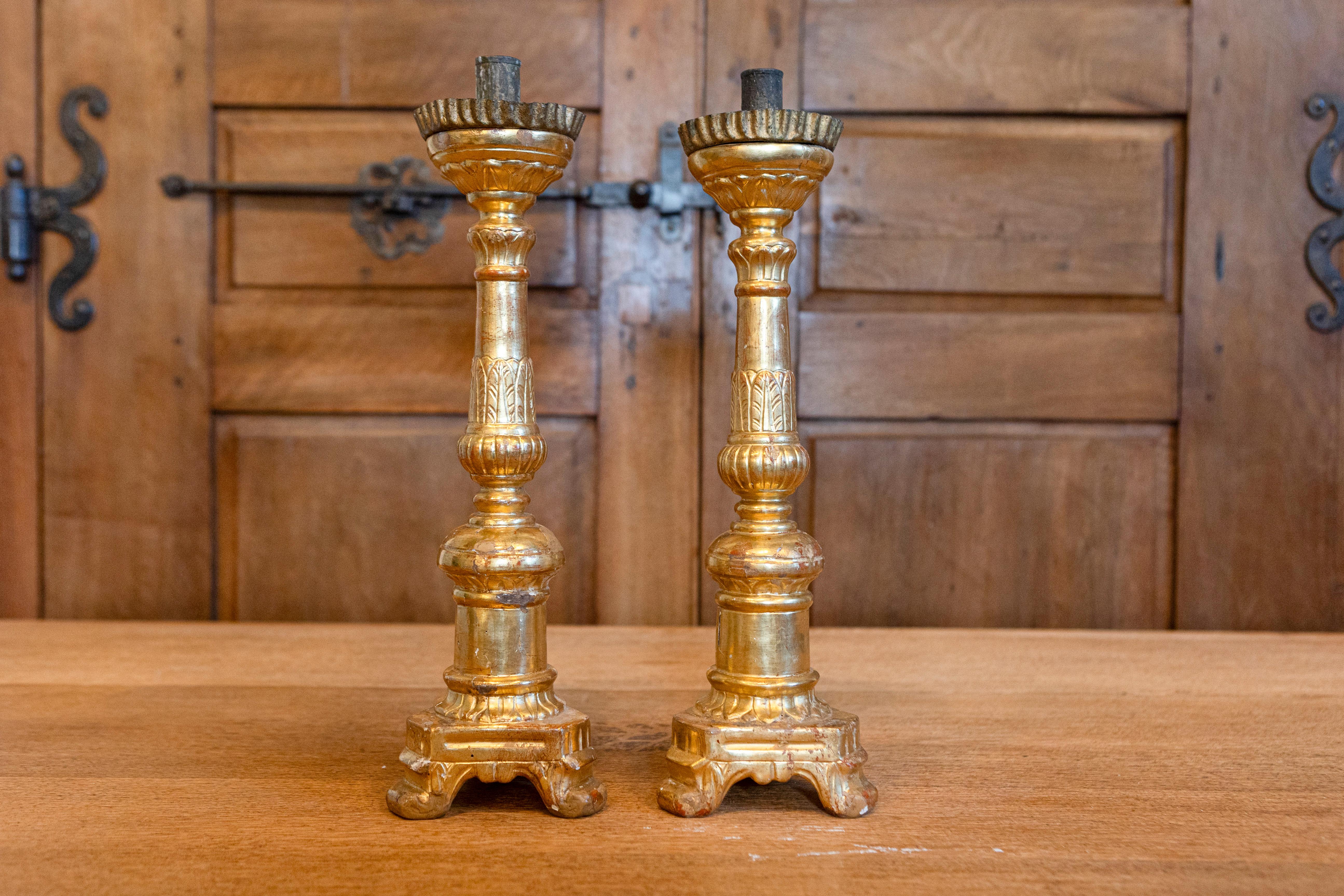A pair of Italian Louis Philippe carved giltwood candlesticks from the mid 19th century with foliage and tripod bases. This exquisite pair of Italian Louis Philippe carved giltwood candlesticks from the mid-19th century epitomizes elegance and