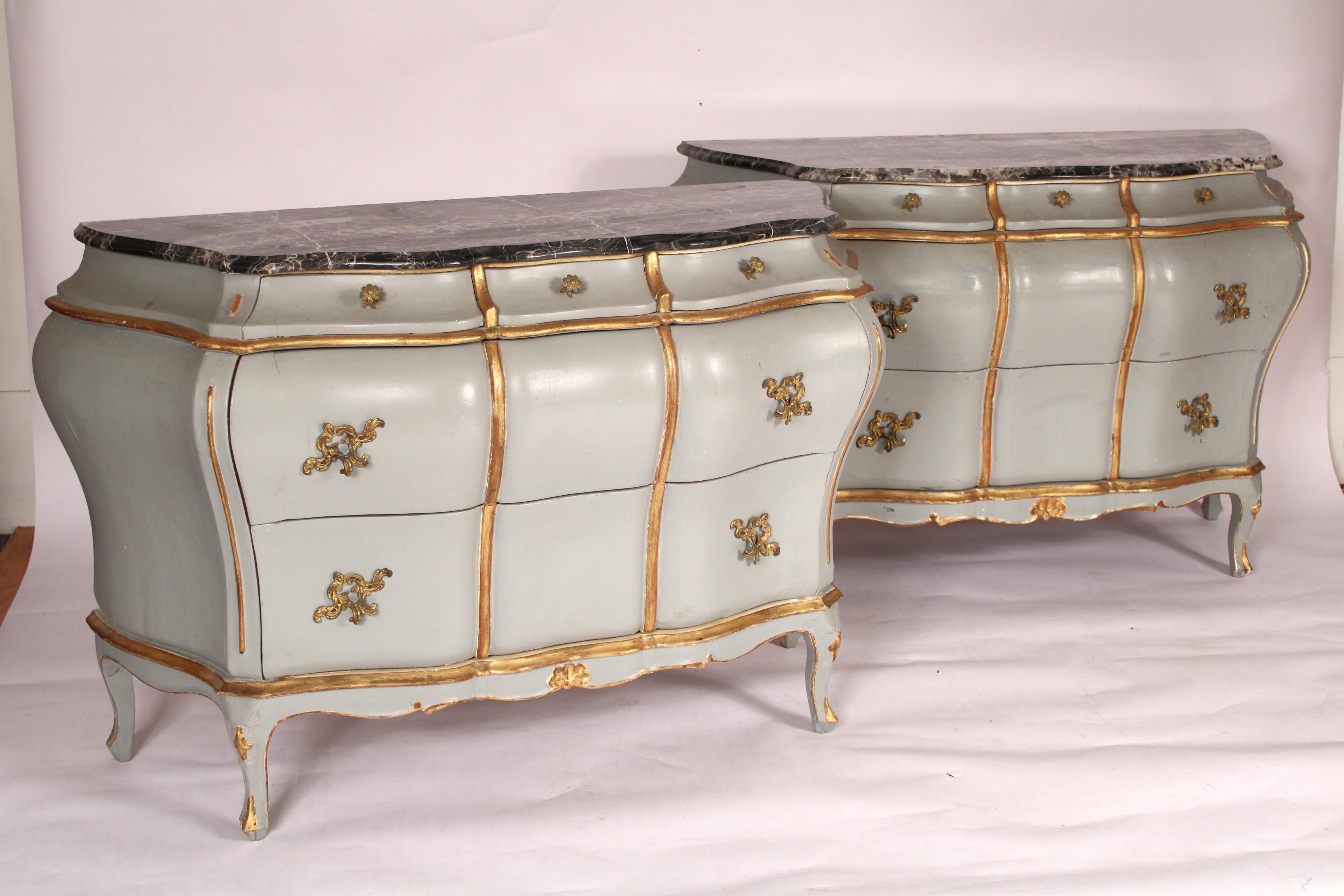 Pair of Italian Louis XV style painted and gilt (gold leaf) decorated bombe chest of drawers with marble tops, circa 1930-1950. Each chest of drawers with a black and white marble top with ogee front and side edges, 3 top drawers and two lower