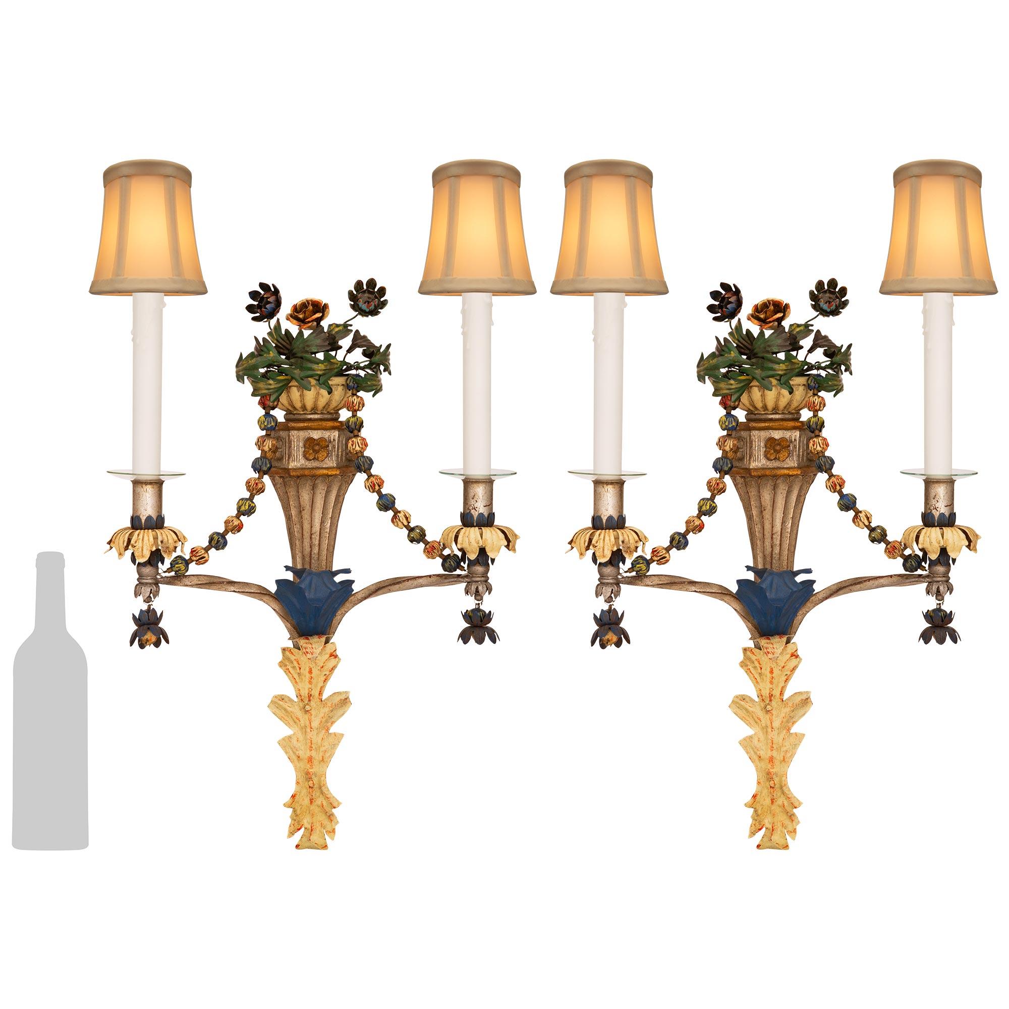 A whimsical and most lovely pair of Italian Turn of the Century Louis XVI st. patinated wood and Gilt Tole sconces. Each most attractive and colorful two arm sconce with its original patination is centered by a patinated Tole acanthus leaf bottom