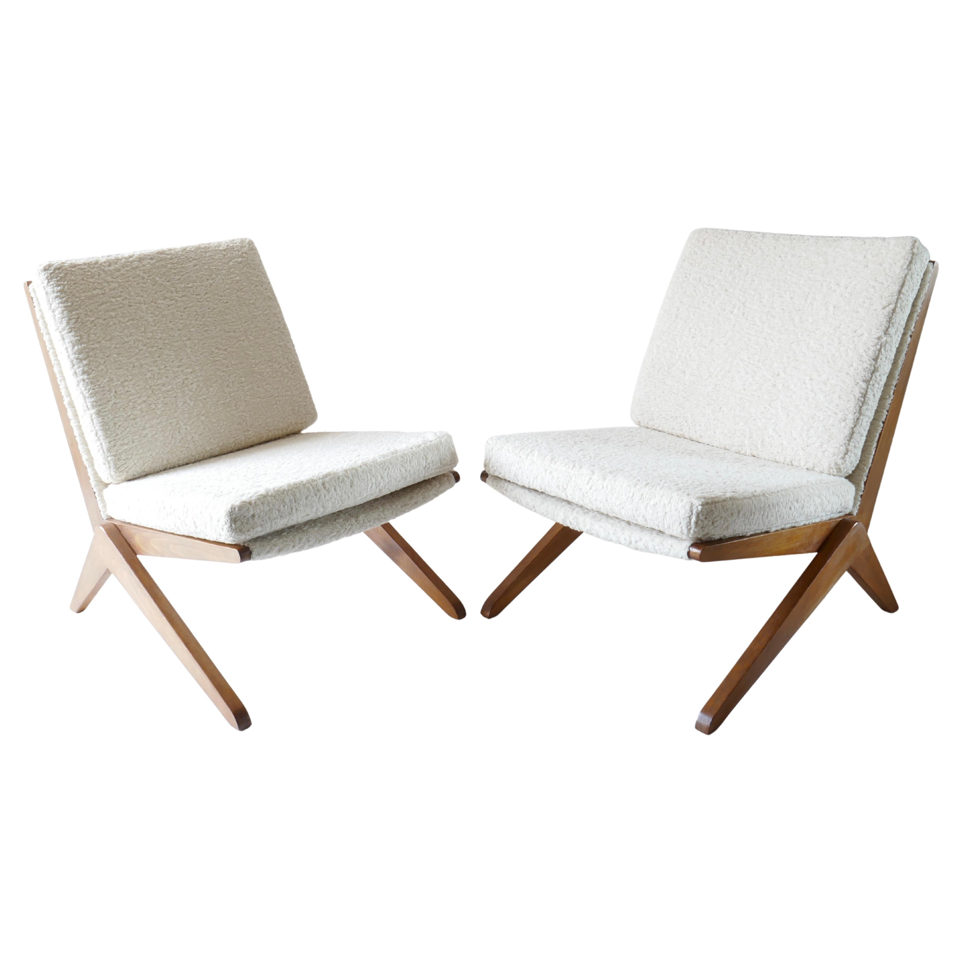 An elegant pair of vintage lounge chair designed in Italy in the 1960s. The minimalist lounge chairs feature a sculpted wood frame with seats and seats base upholstered in white cream boucle. The modern design scissor-like wood frame creates a