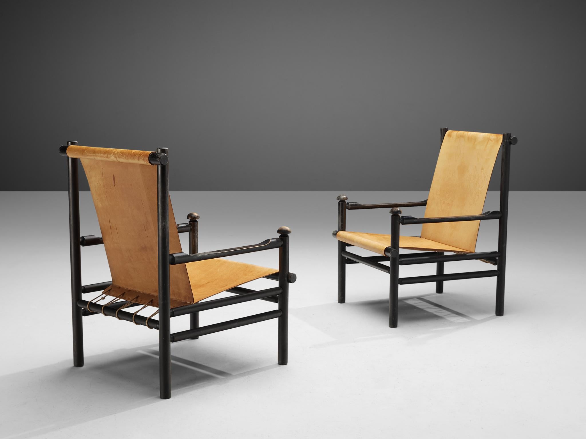 Pair of lounge chairs, cognac leather and black stained wood, Italy, 1950s. 

These chairs embody a strong and angular frame, while also offering a spacious feel due to the open design and light color leather seating. The visible joints are a design