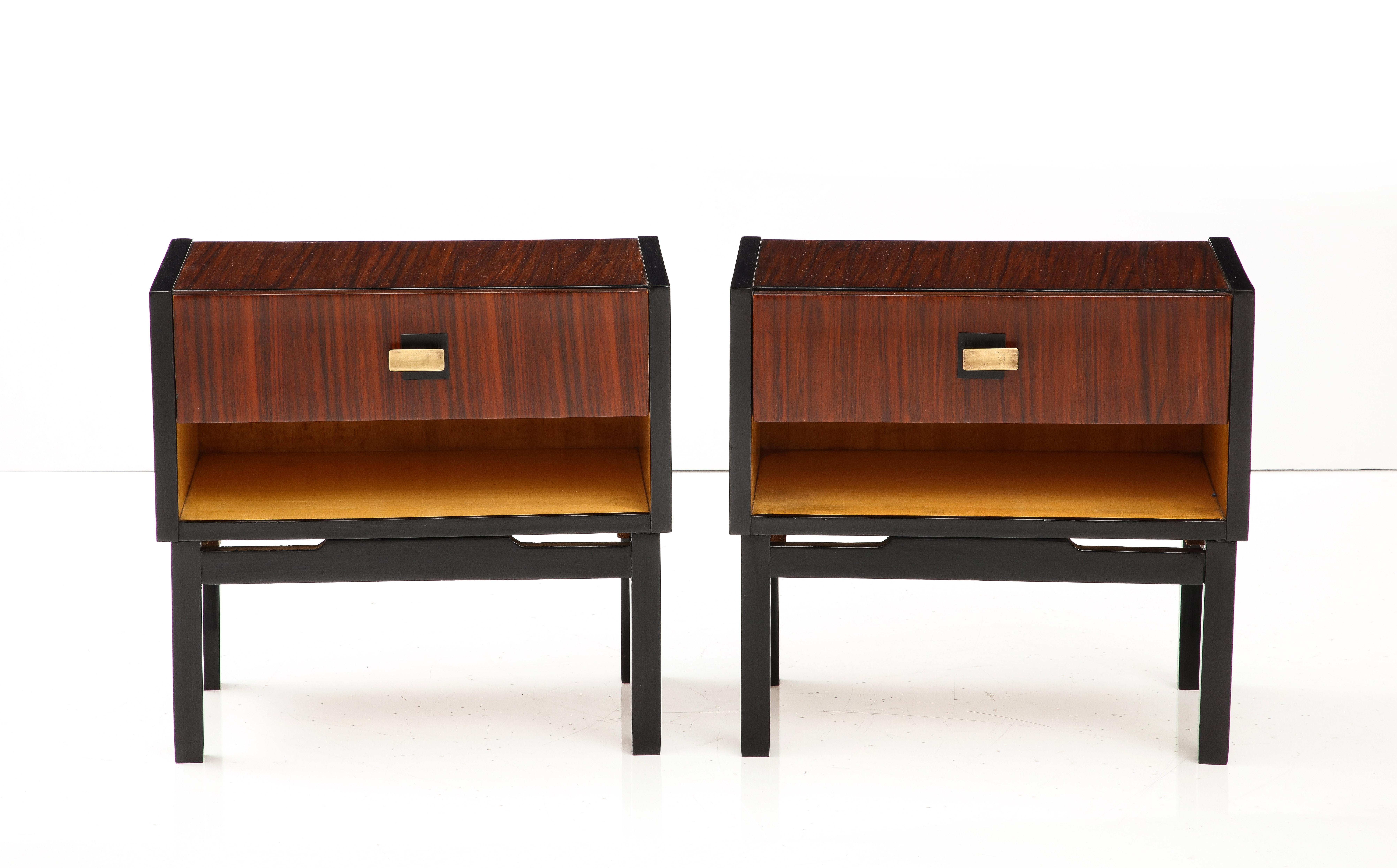 A fine pair of Italian macassar ebony bedside cabinets or end tables. The surface and sides are covered in a macassar ebony veneer and supported on square lacquered and ebonized legs. With one single drawer, featuring elegantly shaped brass handles