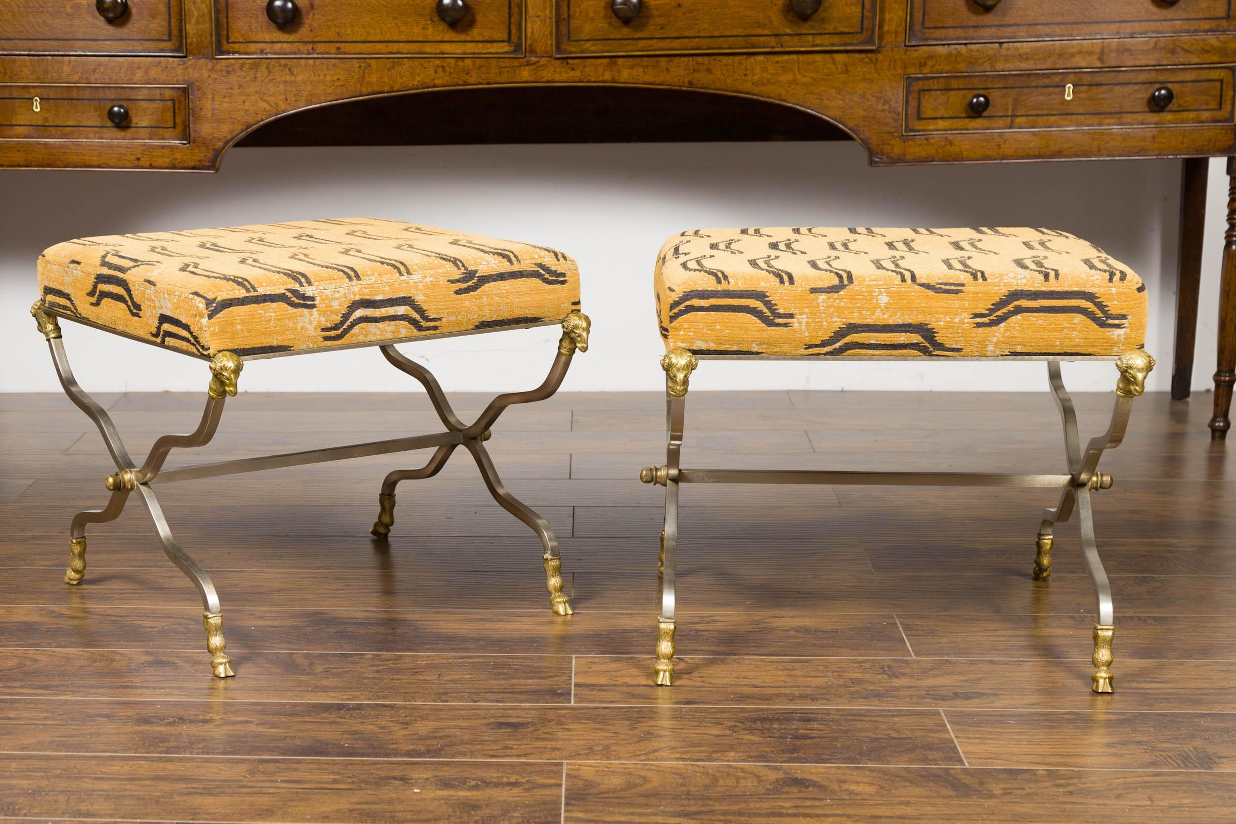 A pair of Italian Maison Jansen style steel and bronze stools from the mid-20th century, with rams' heads and upholstered seats. Born in Italy during the midcentury period, each of this pair of stools features a square upholstered seat, resting on a