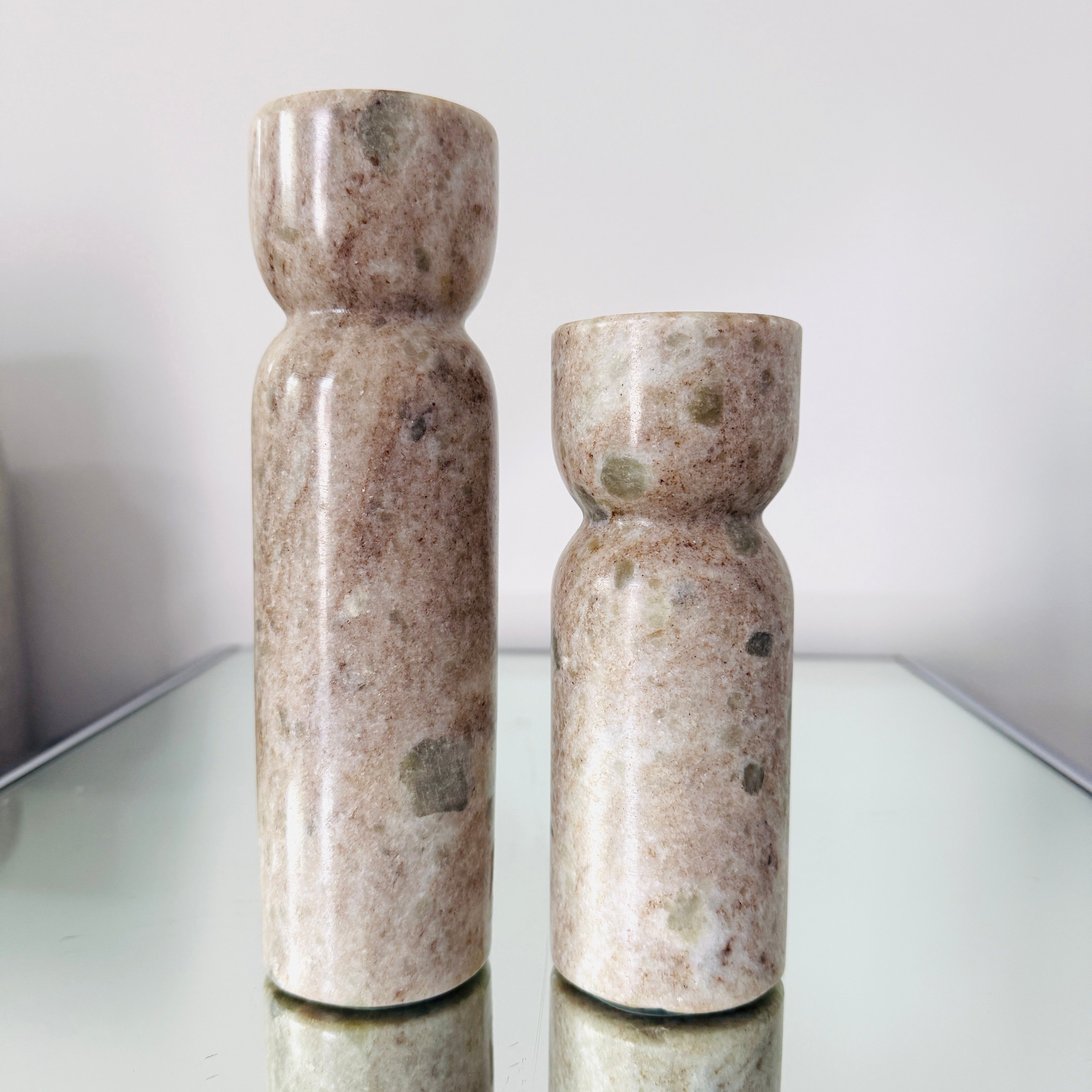 Pair of modernist candlesticks made of handcrafted marble in hues of taupe with spotted sage green accents. The pair includes 8 inch candle holder and 6 inch candle holder, both with polished finishes.