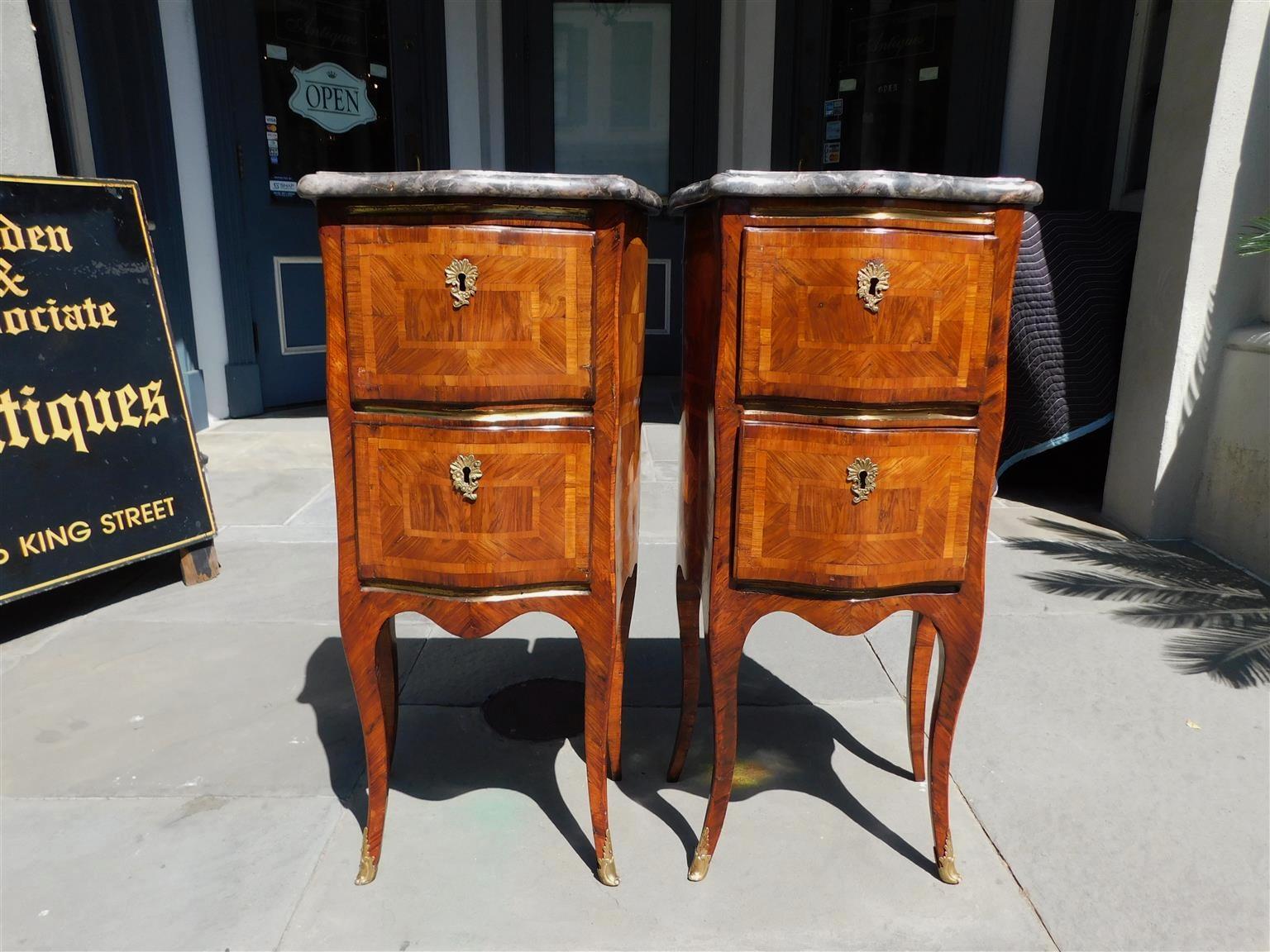 Pair of Italian marble top marquetry inlaid serpentine two drawer commodes with brass banding and foliage escutcheons, interior locks with key, and terminating on shaped cabriole legs with brass foliage capped feet, Late 18th century.