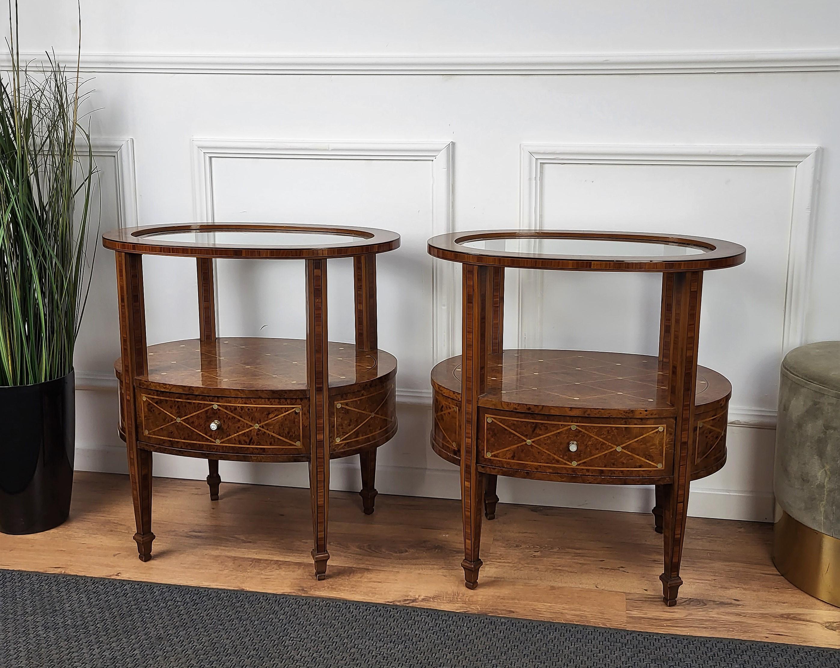 Pair of lovely Italian inlay marquetry and mother of pearl decor night stands or side tables. These beautiful oval shaped tables have a top glass part and on the lower tier a second shelf and a drawer. The tables are raised on four tall and slender