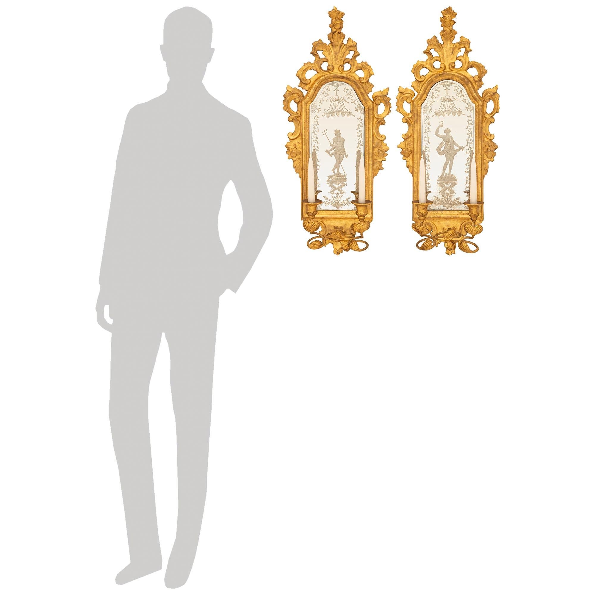 An exquisite and extremely decorative pair of Italian mid 18th century Baroque Period Giltwood mirrored sconces. Each wonderful Venetian st. two arm sconce has an etched mirror plate, one displaying the Greek god of the sea Neptune, and the other