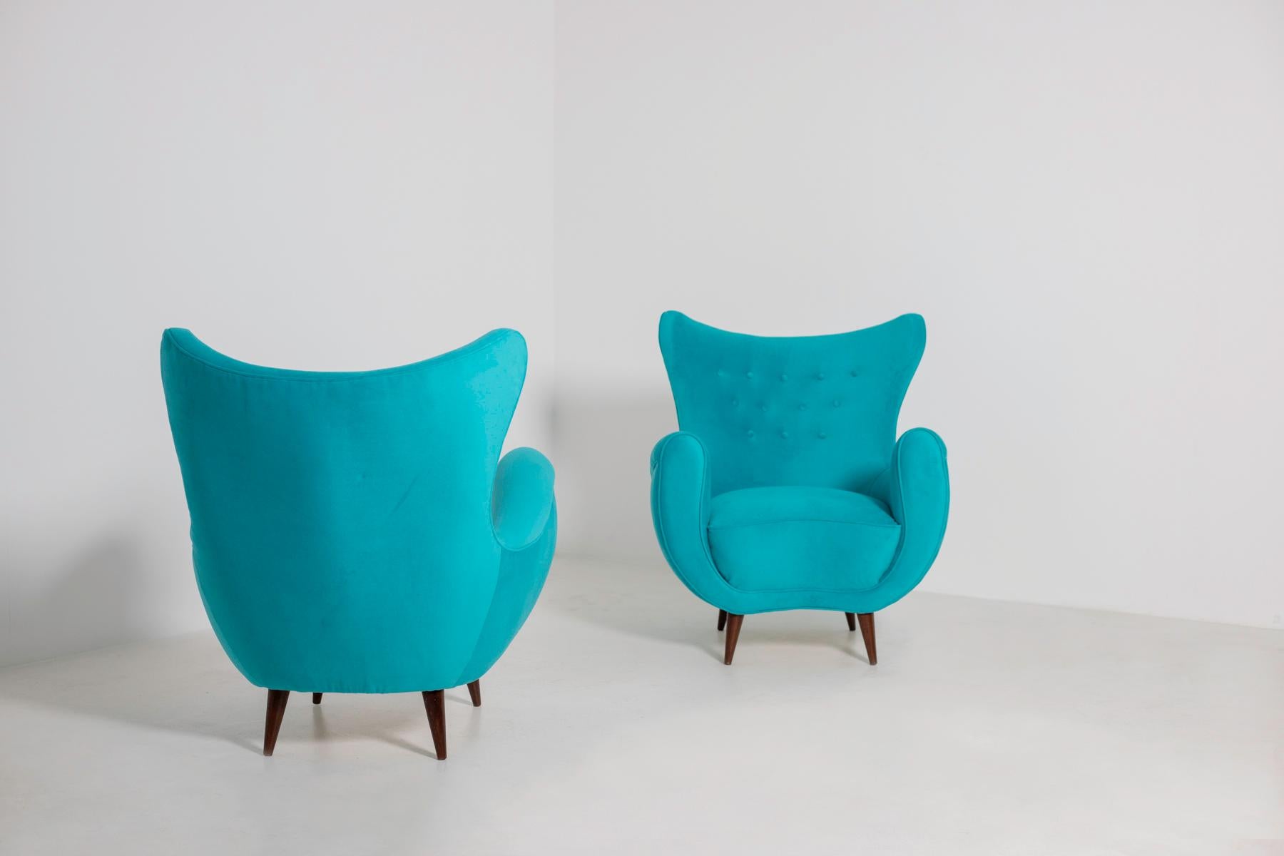 Elegant pair of Italian midcentury armchairs from the 1950s. The pair of armchairs has been restored in an elegant and refined Italian blue velvet. The peculiarity of the seat is its enveloping semi-curved backrest that gives a perfect harmony to