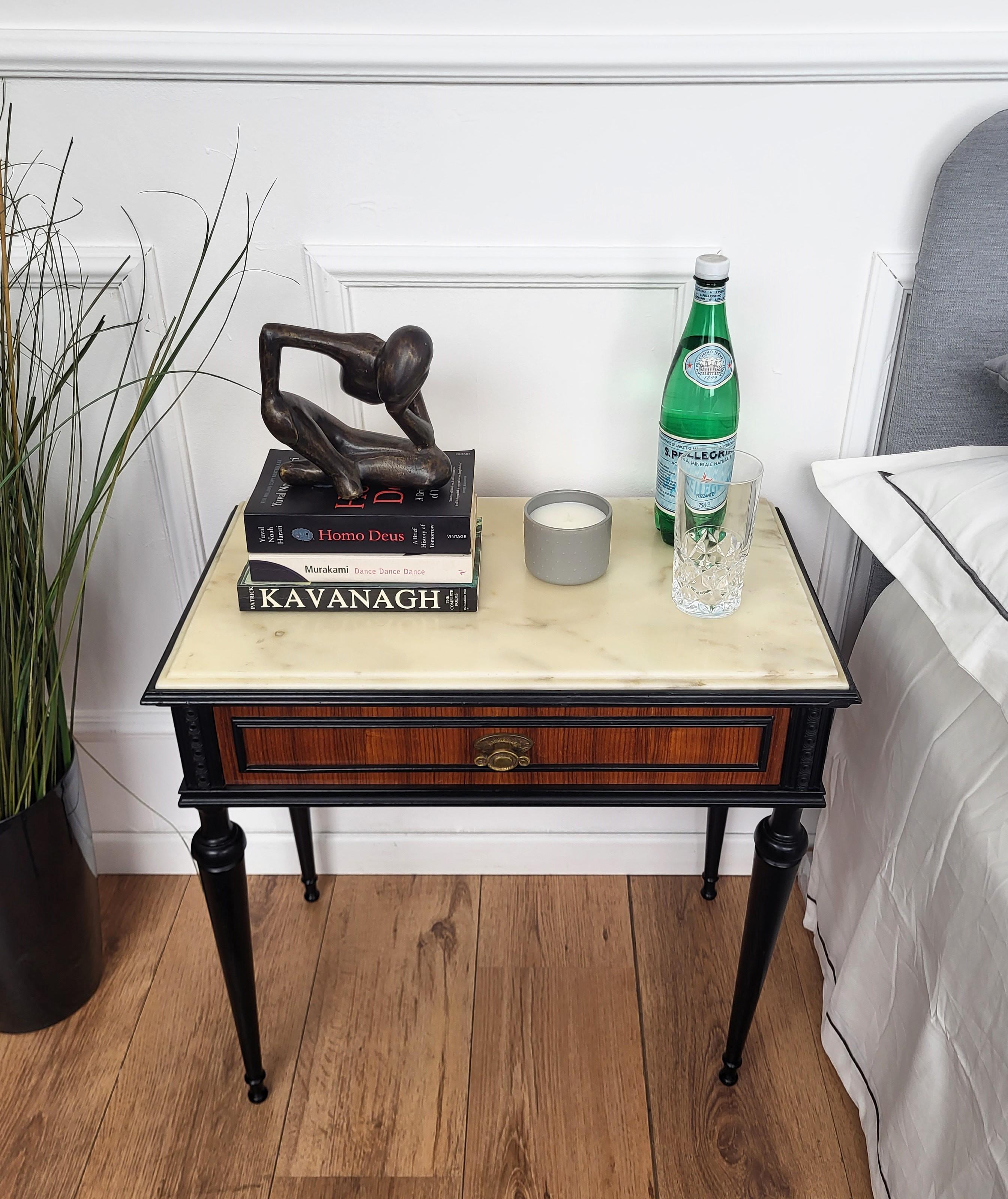 Very elegant and refined Italian 1950s neoclassical pair of night stands bed side tables with greatly carved detailed and decorated wooden structure, wood veneer decorated front drawer and beveled white marble top with brass details and fluted