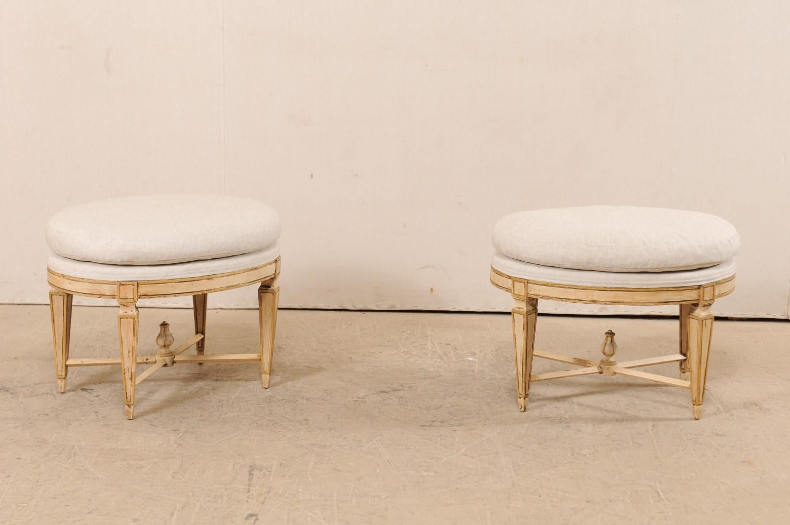 A pair of antique Italian stools with unique oval-shaped seats and carved wood frame. This fabulous pair of stools each feature oval-shaped upholstered seats, raised on four spaded legs, which are supported with an x-stretcher adorn with a raised
