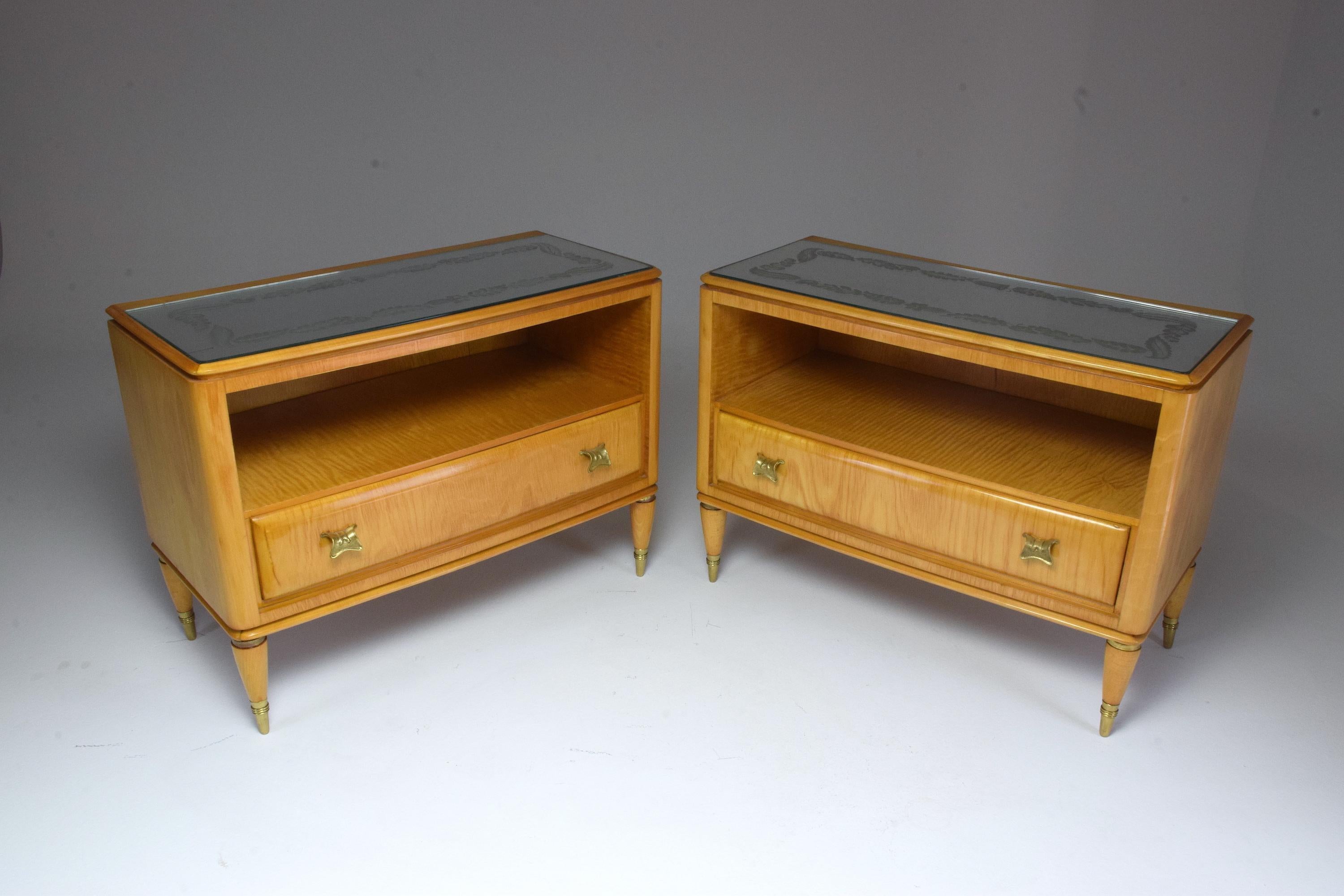 Set of two 20th century vintage Italian nightstands or bedside cabinets, circa 1940s composed of the original flower patterned engraved glass tabletop, a light brown maple wood structure and cone shaped legs with brass details. It is composed of a