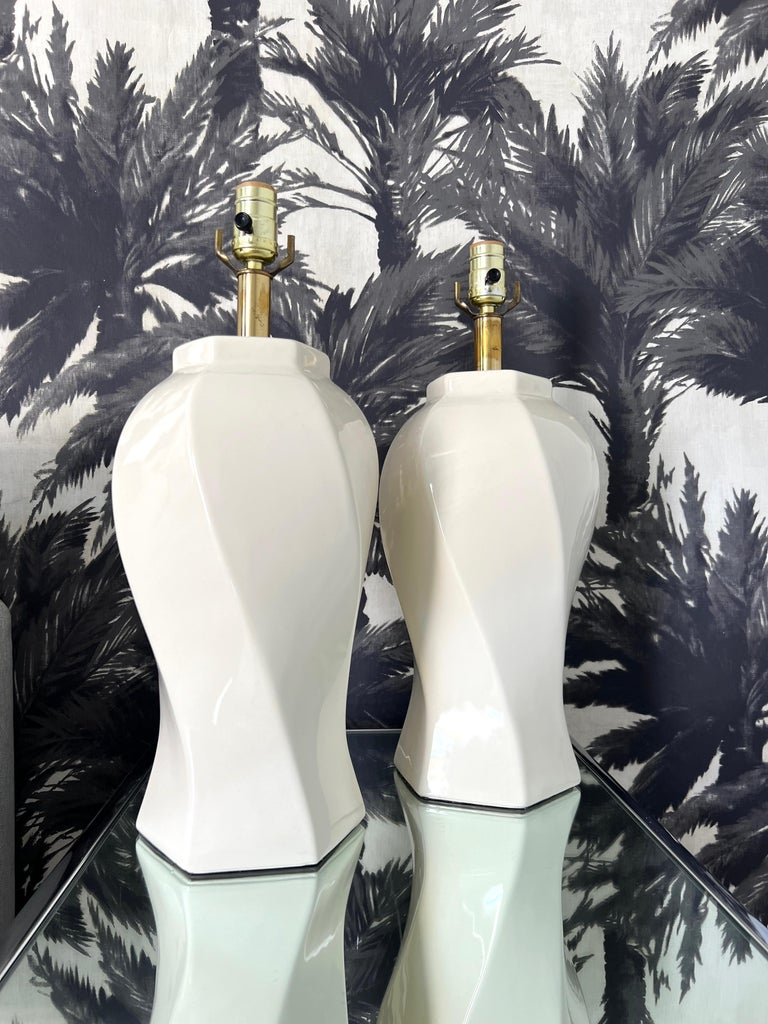 Pair of 1970's Italian ceramic lamps with chic Hollywood Regency inspired design. 
The lamps have elegant urn forms with stylized swirl design in ivory or light cream colored glaze. Fitted with brass metal stems and includes white linen drum shades.