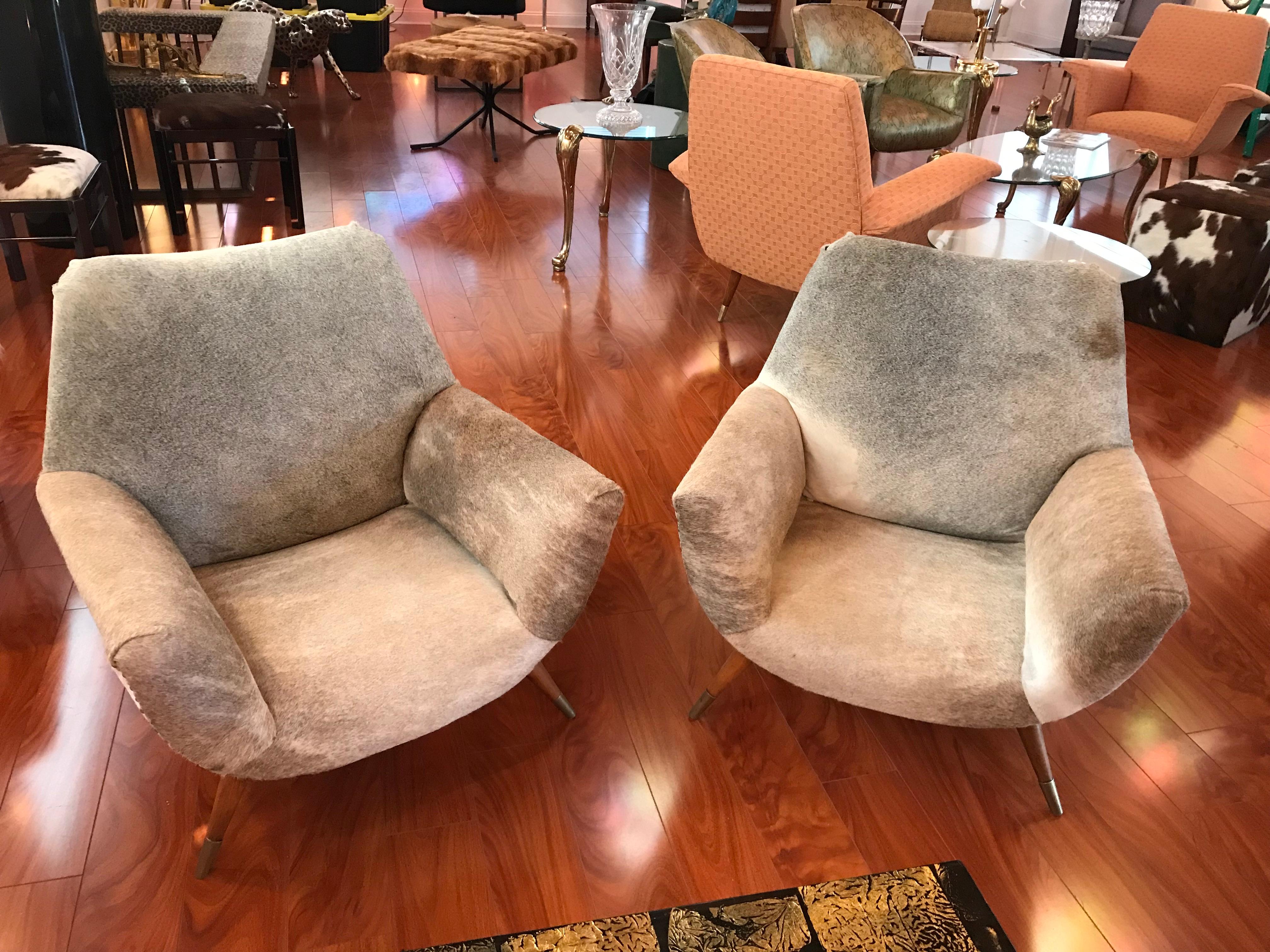 A pair Italian Mid-Century Modern club chairs covered in cow hide having nailheads, circa 1960. These are great for any room and the cowhide is in amazing condition. The club chairs are a little lower to the floor with a Seat height of 12.5 inches.