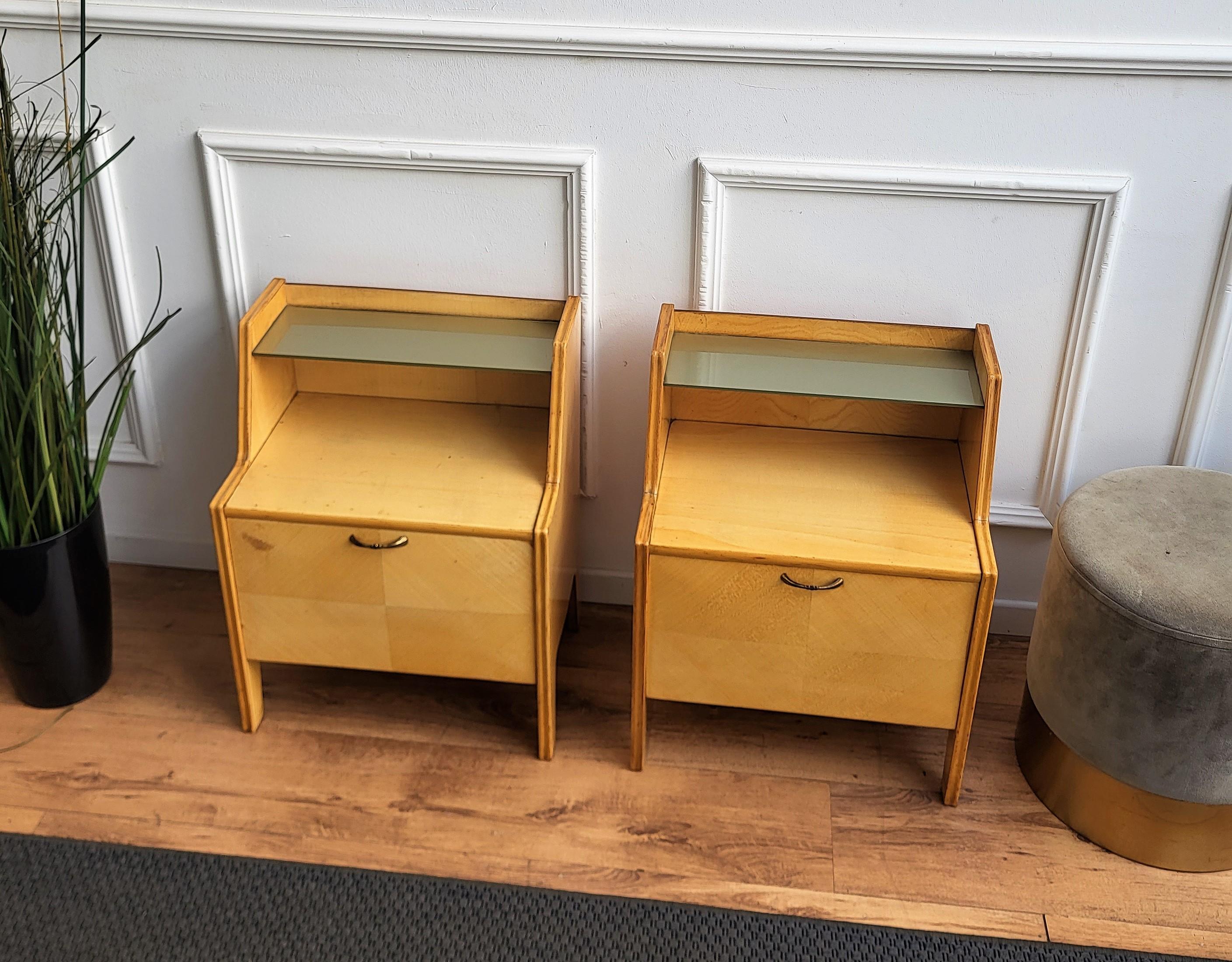 Very elegant and refined Italian 1950s Mid-Century Modern pair of bedside tables with great design of the white maple wood on the frontal door with brass handles and glass shelf. The great vintage shape and design, as well as the brass details make