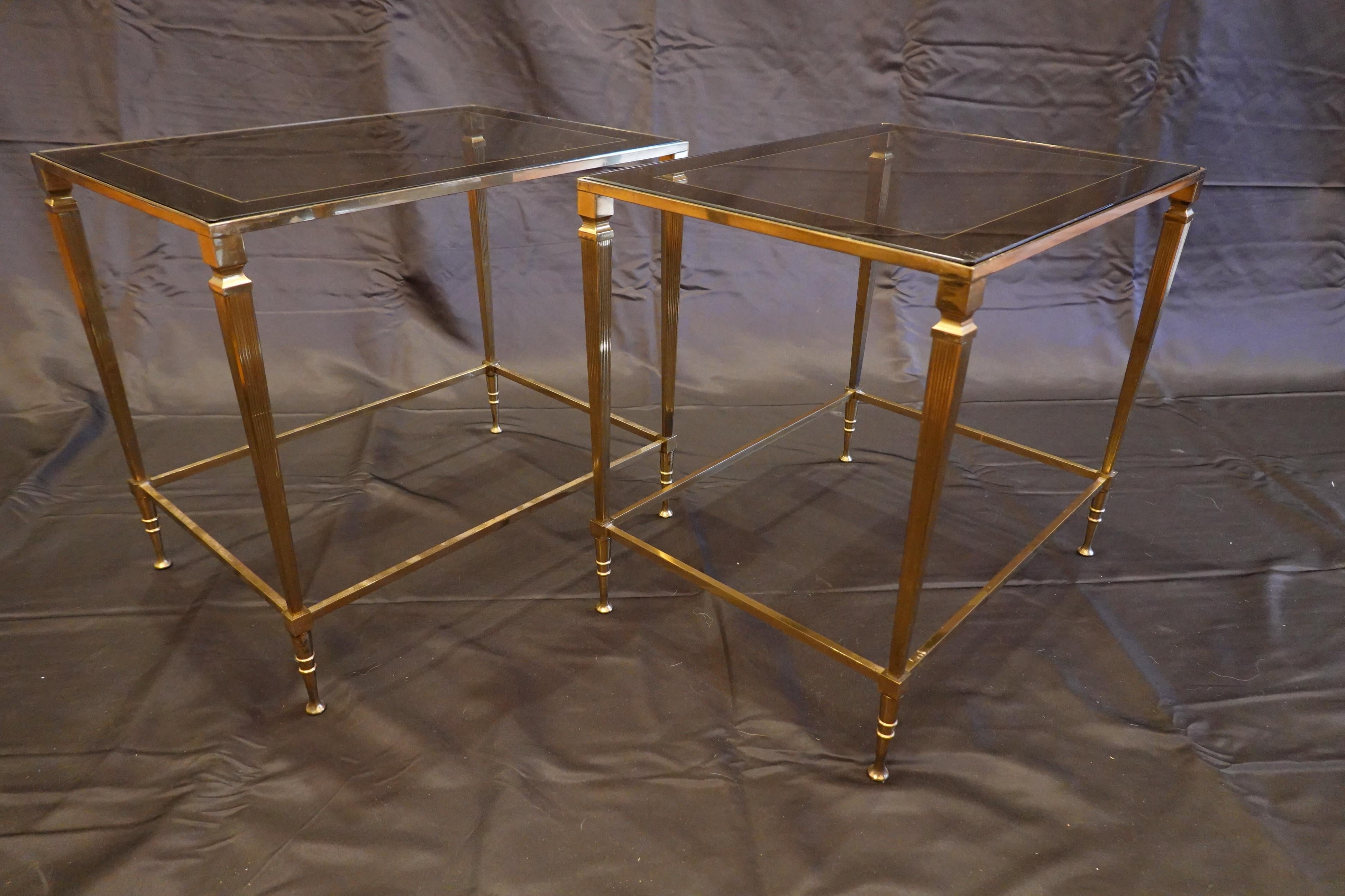 Paire de tables d'appoint italiennes en laiton doré avec dessus en verre, (circa 1970). Ces tables élégantes sont dotées de plateaux en verre légèrement fumé avec des bandes argentées sur le pourtour, et de simples pieds cannelés se terminant par