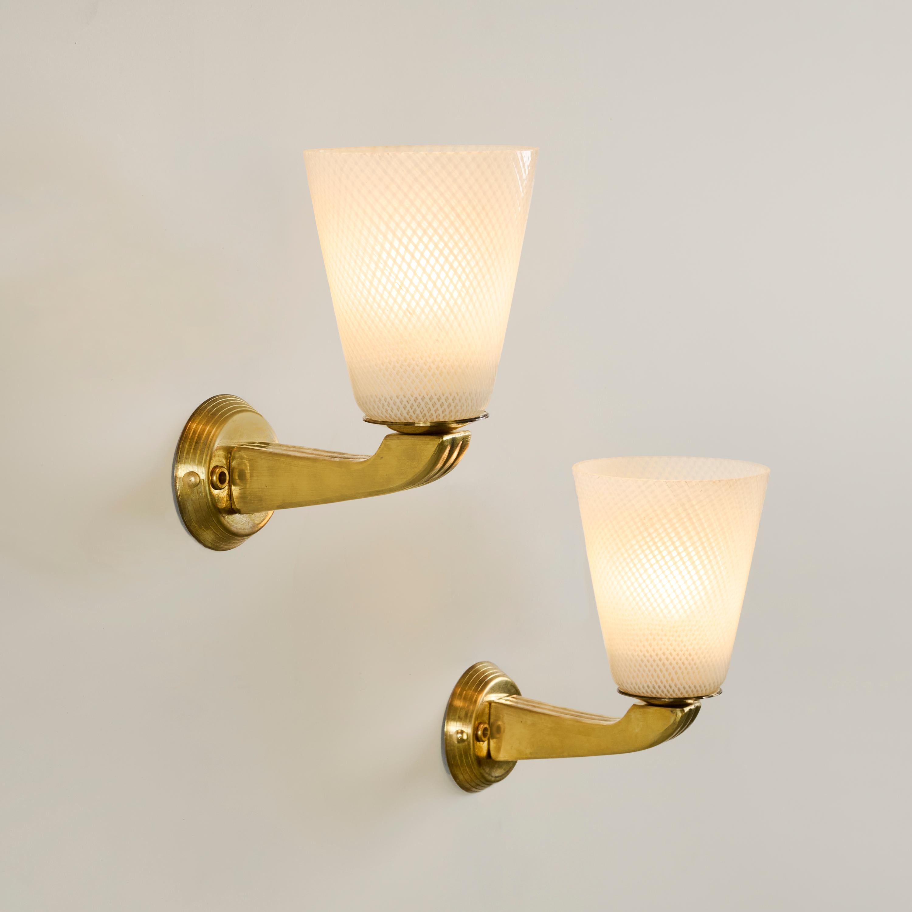 Attraente coppia di applique in vetro di Murano Reticello con braccio decorativo in ottone e piastra posteriore circolare. Emana un'incantevole luce calda.
