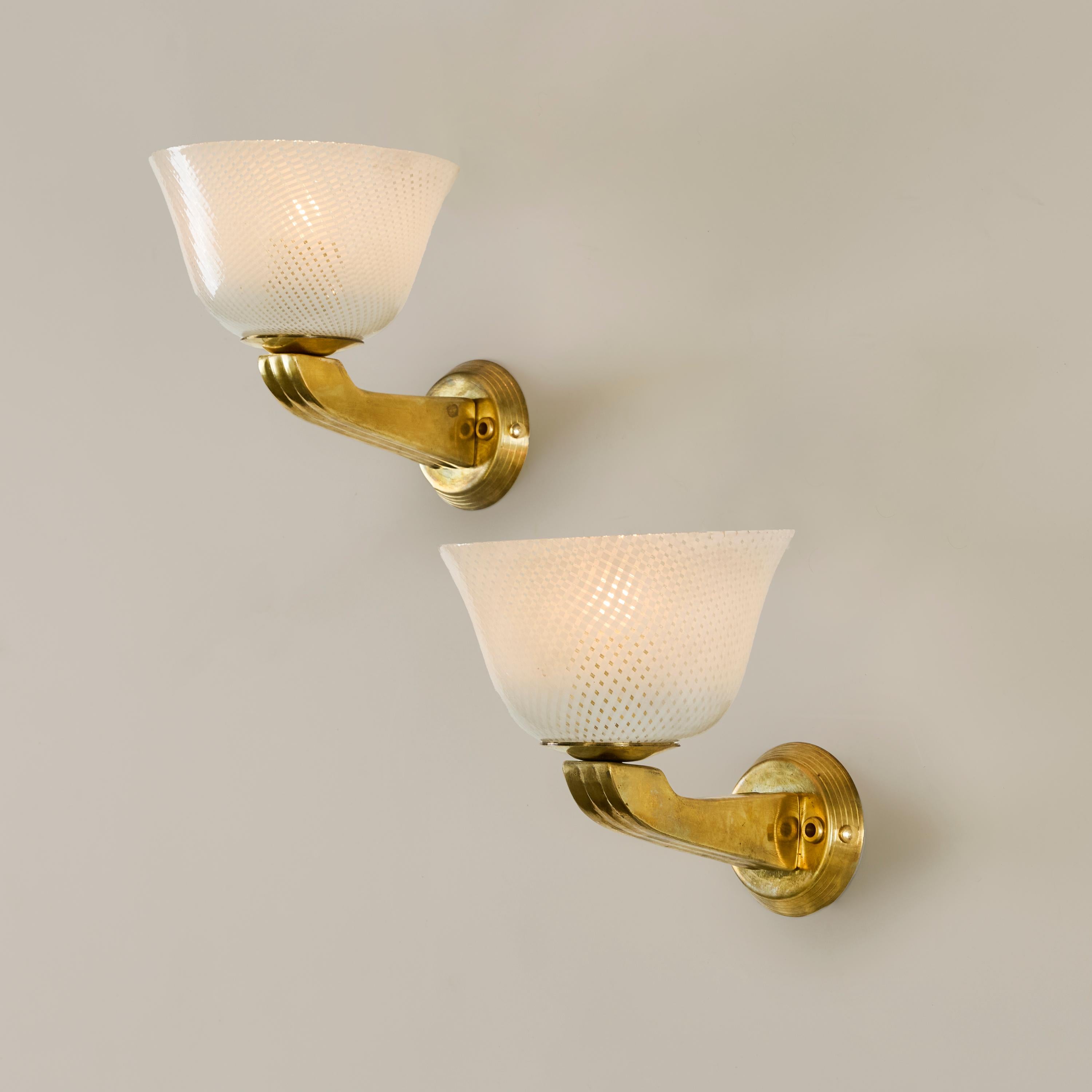 Attraente coppia di applique in vetro di Murano Reticello con braccio decorativo in ottone e piastra posteriore circolare. Emana un'incantevole luce calda.
