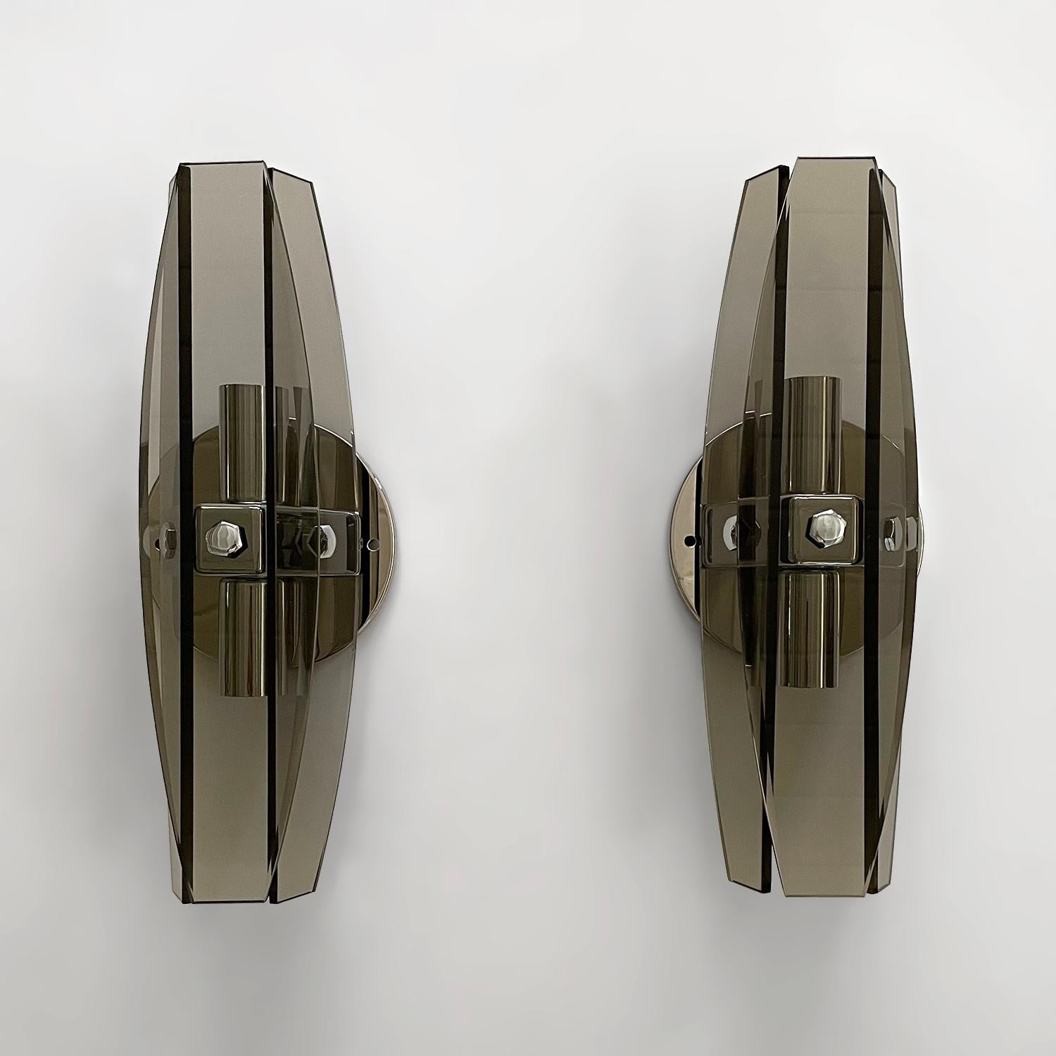 Paar italienische Rauchglas-Wandleuchter aus der Mitte des Jahrhunderts
Italien, ca. 1960er Jahre
Drei abgeschrägte Glasstücke werden aufgehängt, um die Lichtquelle zu umschließen
Die Rückwand des Mittelstücks hat zwei einzelne