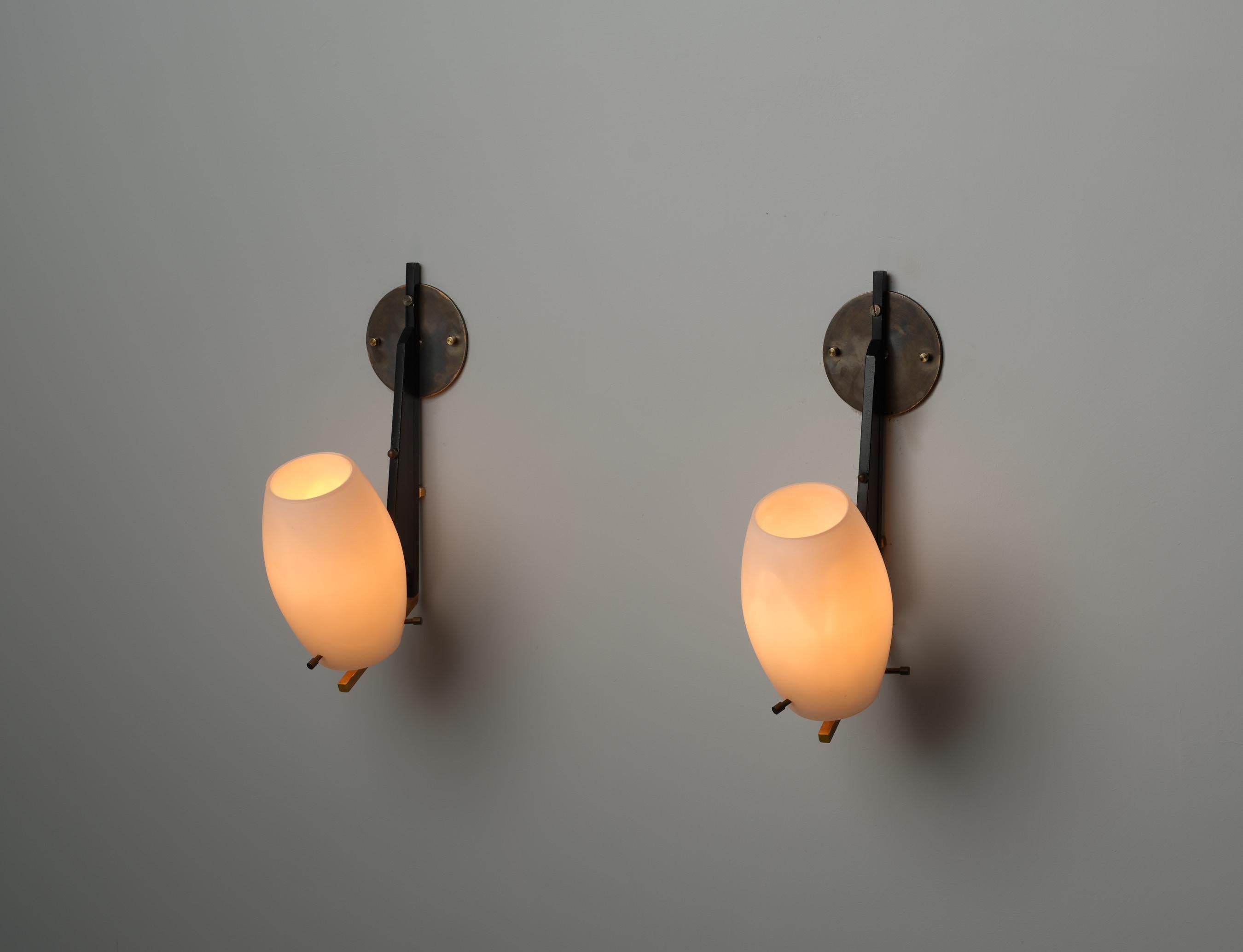 Cette paire d'appliques murales italiennes des années 1950 incarne le design classique du milieu du siècle avec des lignes raffinées et minimalistes. Entièrement fabriquée en laiton, chaque applique combine des éléments en laiton laqué noir et des
