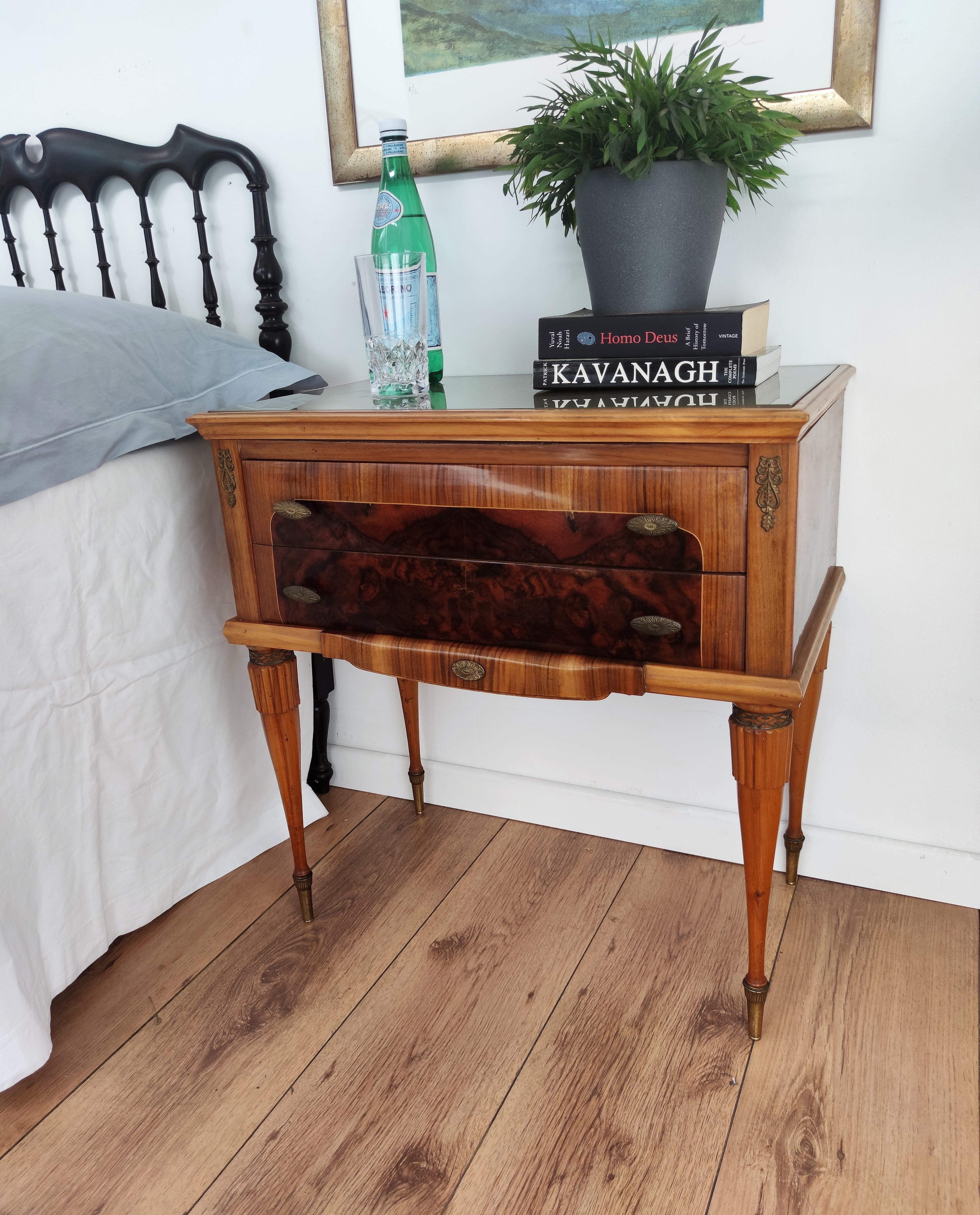 Very elegant and refined Italian 1950s neoclassical pair of bedside tables with inlay walnut veneer wood, 2 drawers with brass handles, carved legs with brass final and lacquered glass top. Those nightstands make a great look in any style bedroom,