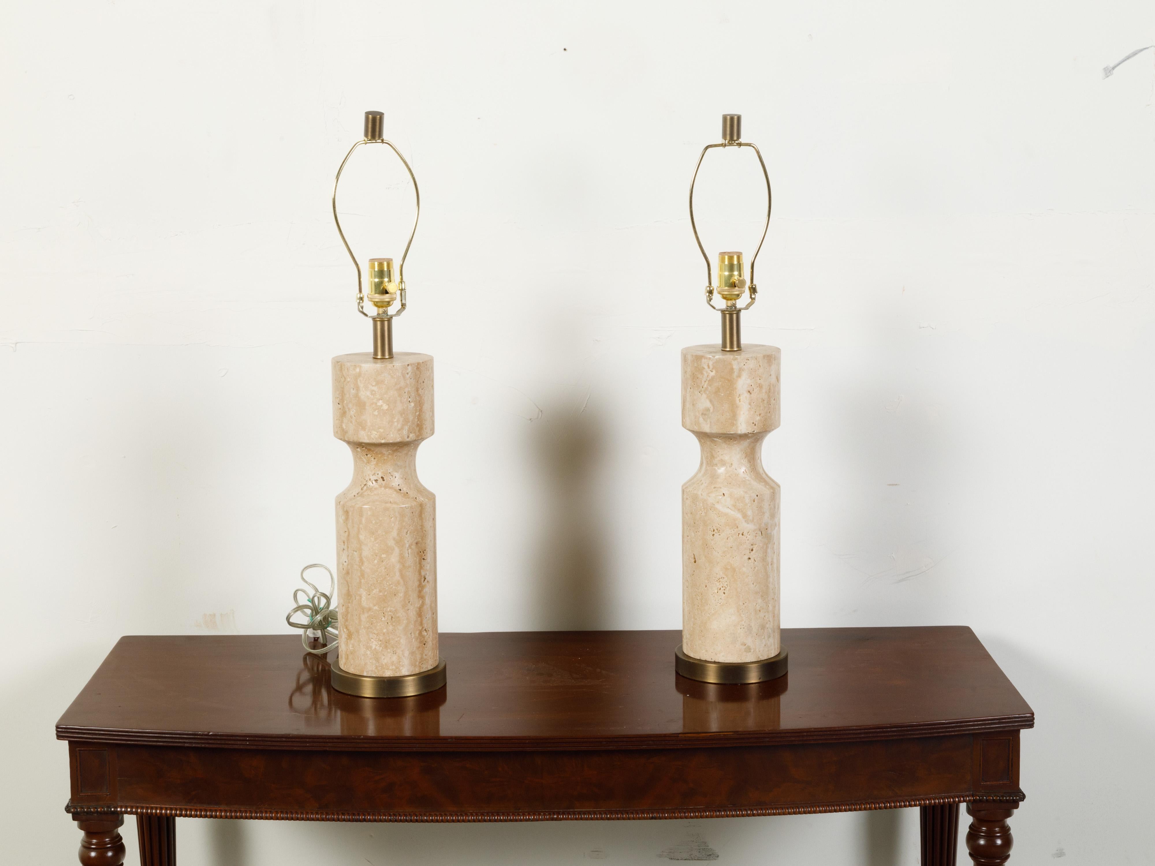 A pair of Italian marble table lamps from the mid 20th century, with circular bases. Created in Italy during the midcentury period, each of this pair of table lamps features a cream toned marble baluster with concave accentuation, resting on a