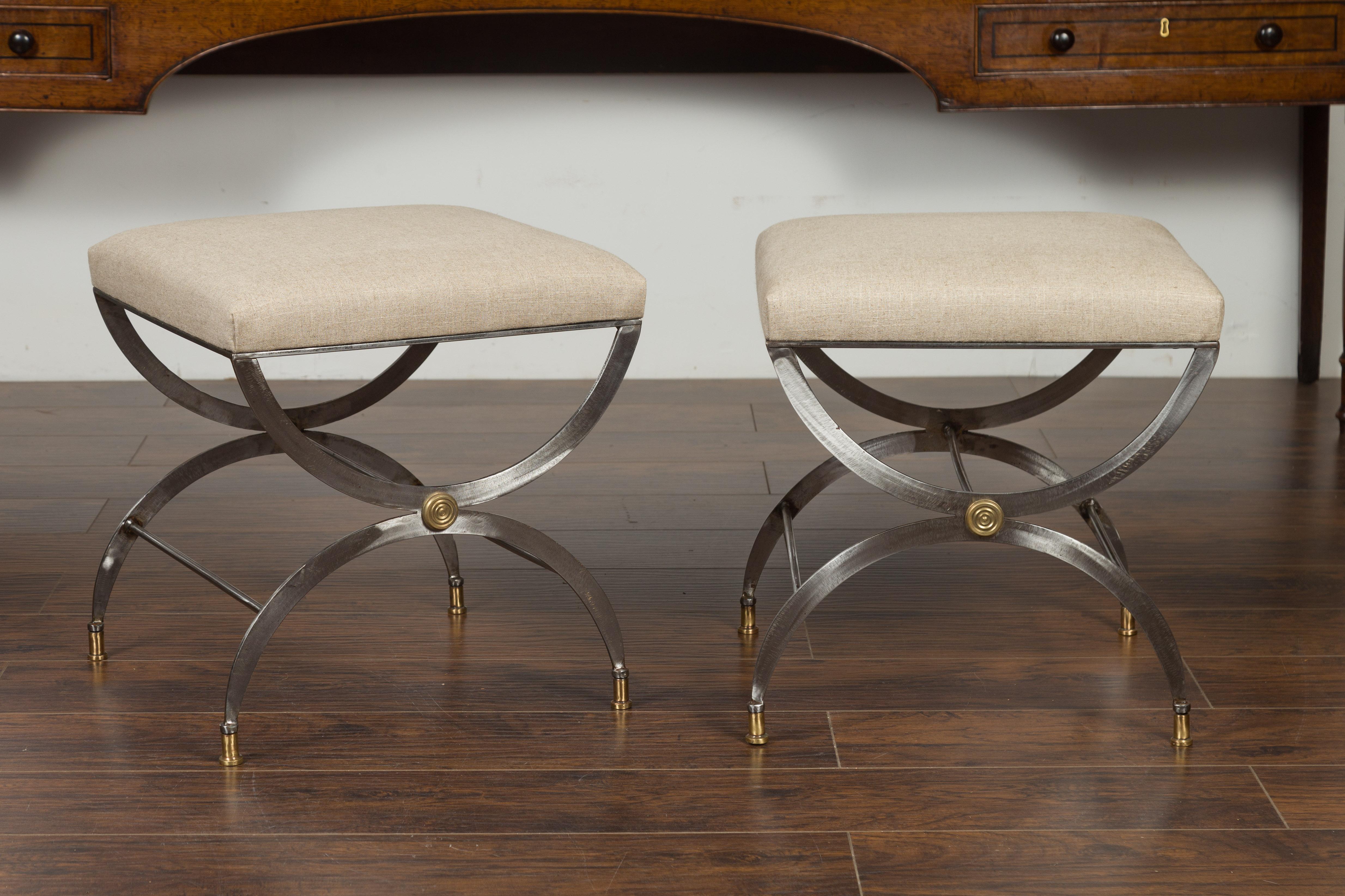 A pair of Italian vintage steel curule stools from the mid-20th century, with brass accents and new upholstery. Created in Italy during the midcentury period, each of this pair of stools captures our attention with its steel and brass structure