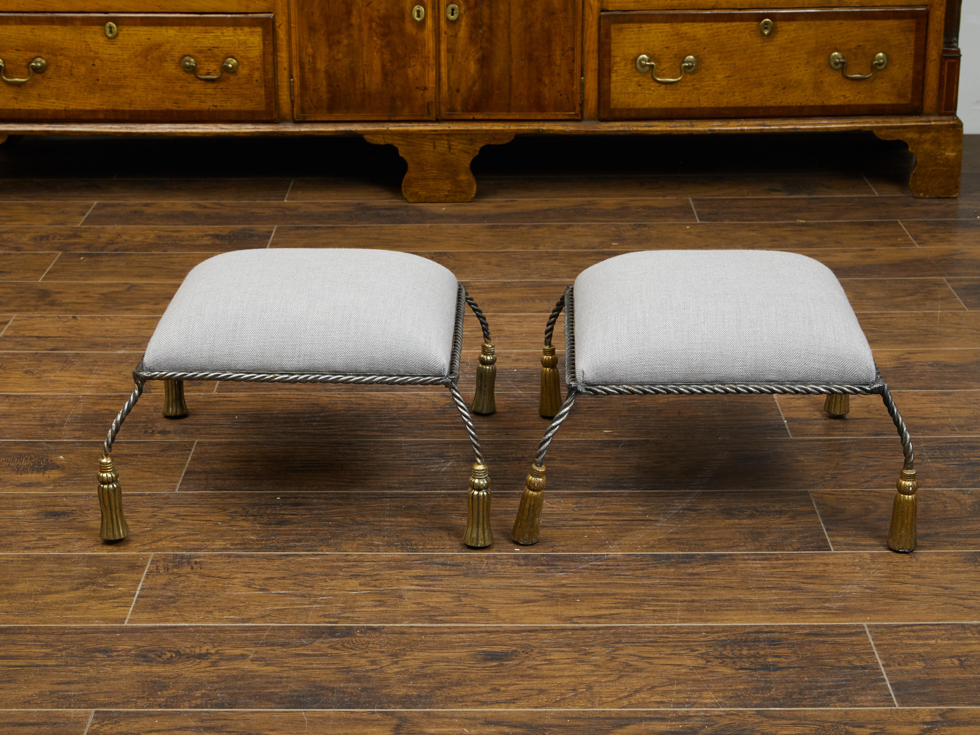 A pair of Italian vintage metal stools from the mid 20th century, with carved wooden tassels and new upholstery. Created in Italy during the midcentury period, each of this pair of stools features a square top reupholstered with a light grey fabric.