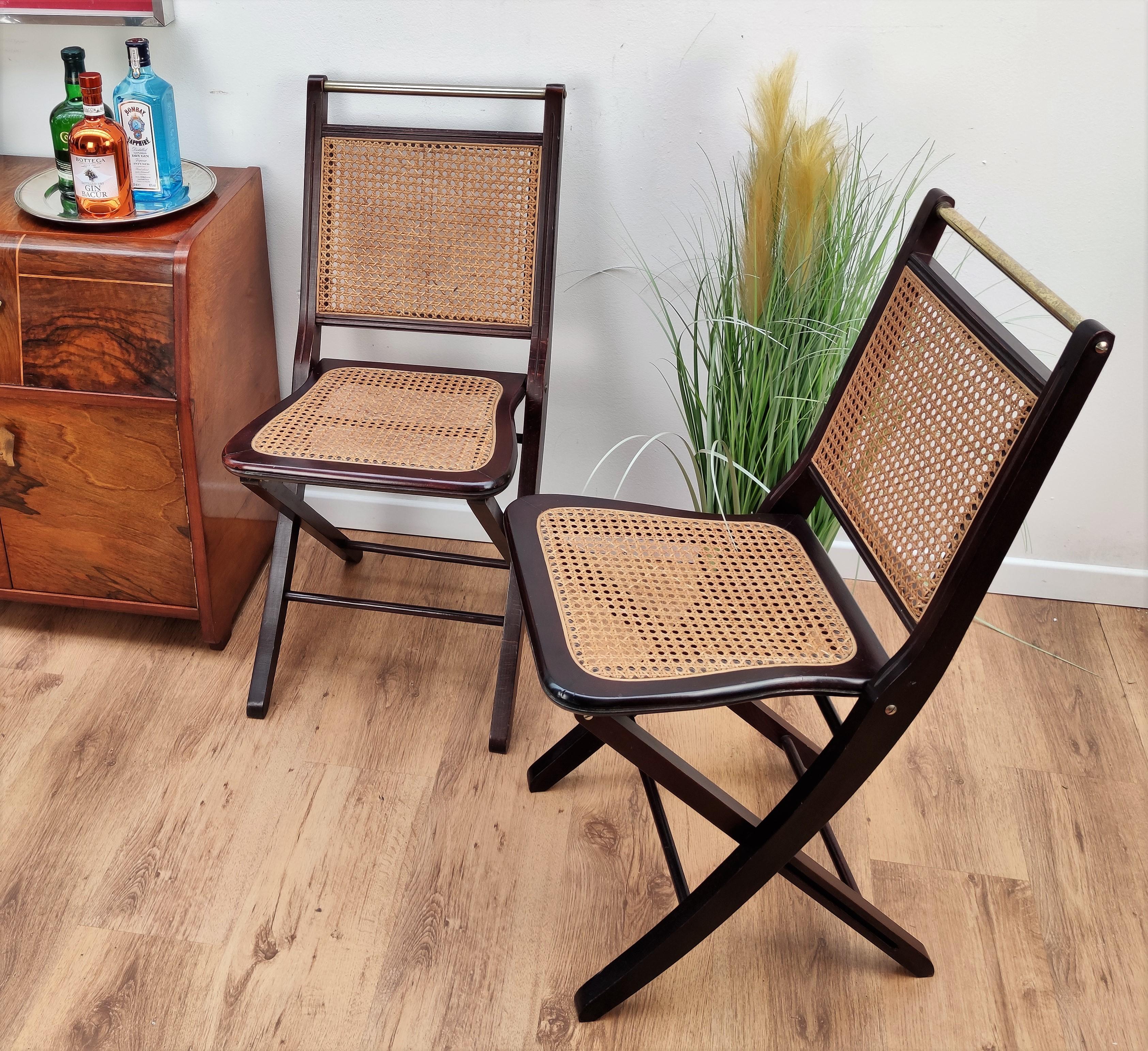 Beautiful pair of Italian midcentury foldable chairs in a solid wood frame structure with brass details and rattan or wicker caned on the nicely shaped seating as well as on the back. In good conditions, ideal as elegant and catchy extra chairs.