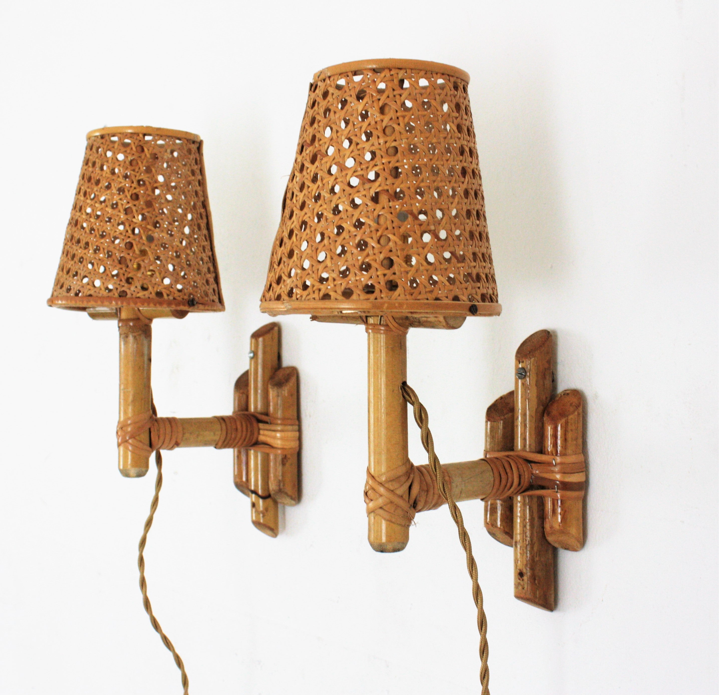 Eye-catching pair of Mid-Century Modern bamboo wall sconces with wicker weave lampshades, Italy, 1960s.
These midcentury wall lights feature backplates made of bamboo canes holding bamboo arms with conical wicker wire lampshades.
They will be the