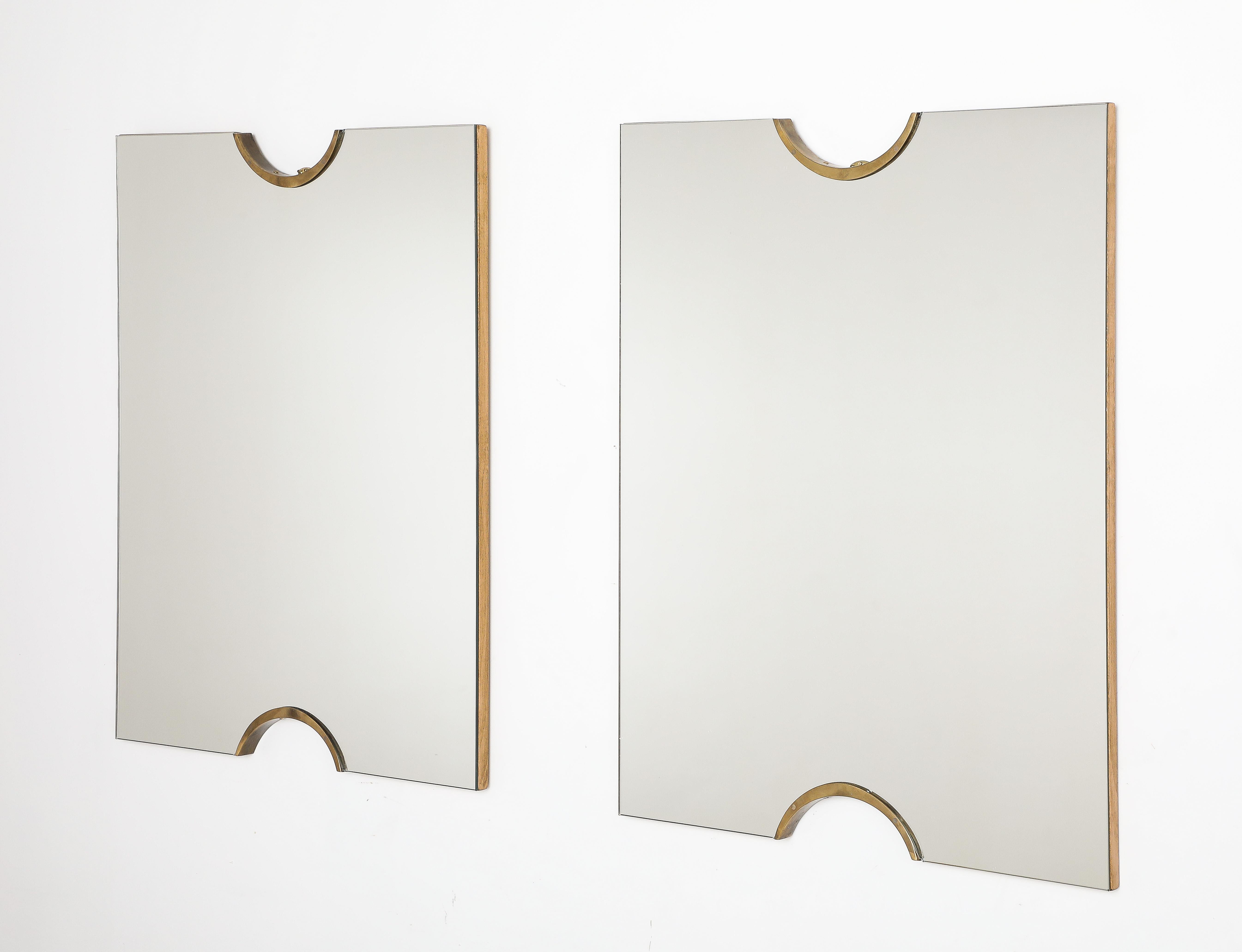 A pair of Italian modernist wall mirrors, the rectangular mirror plate with brass shaped semi-circle motif on the crest and base.  The whole with a chic and streamlined aesthetic with no border or molding interruptions.  Mounted on a wood frame.