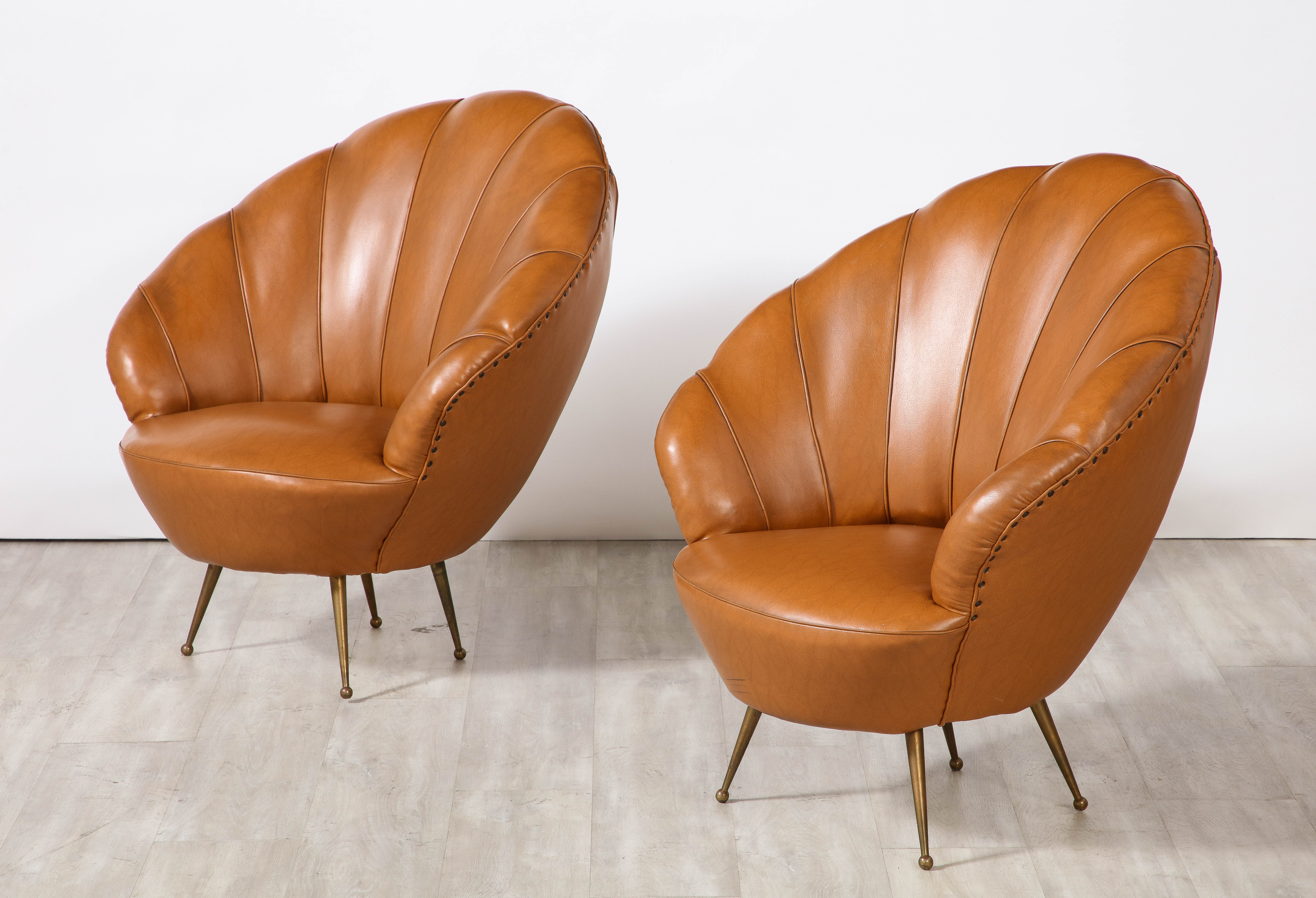 A charming and whimsical pair of Italian 1950's leather lounge chairs with scalloped shaped wide back rests, the rich cognac leather contrasts with the nail head trim and elegantly splayed brass legs. 
Italy, circa 1950.
Size: 34