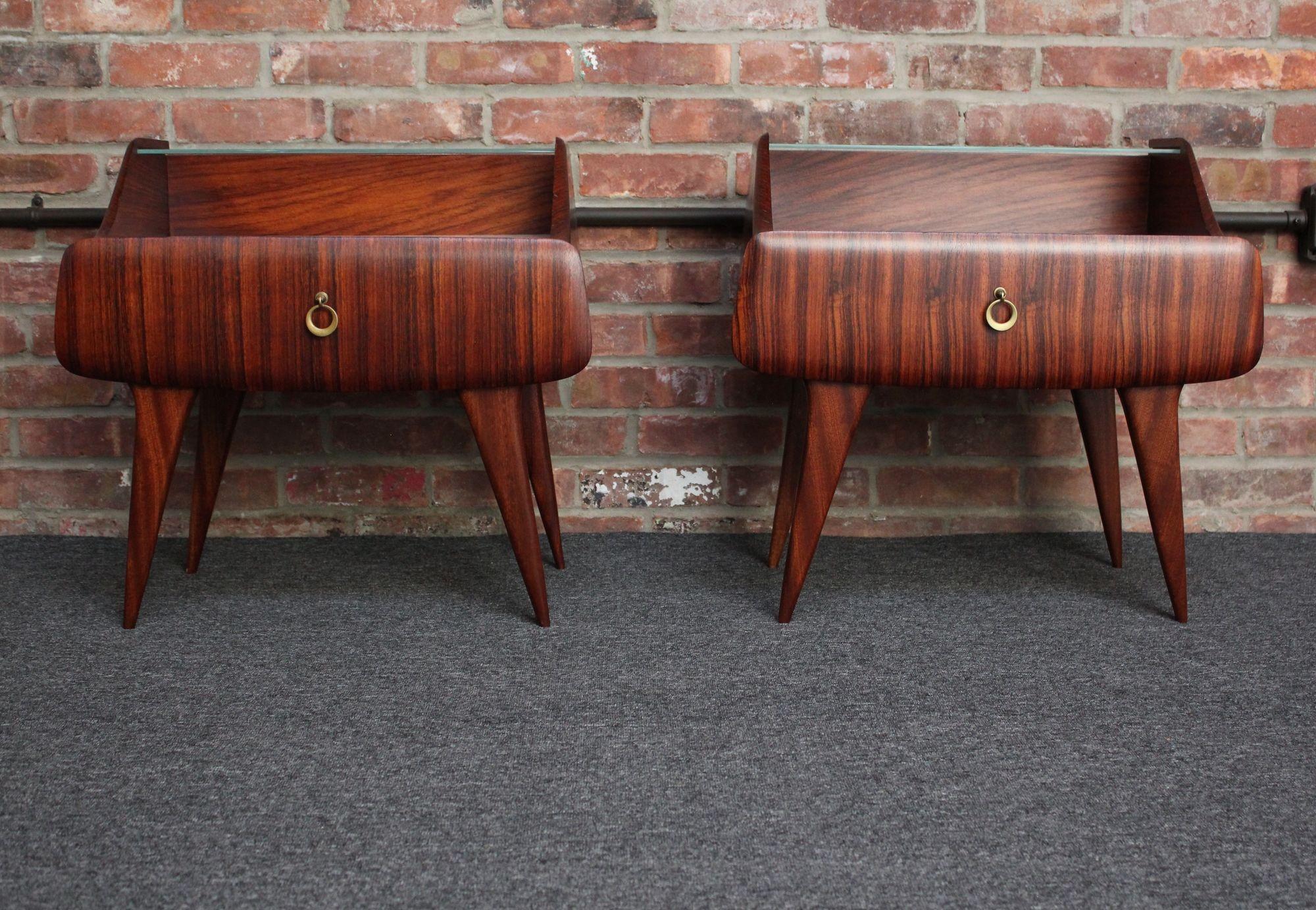Pair of rosewood nightstands/bedside tables with single drawers and brass pulls along with deeply sculpted, splayed legs (ca. 1950s, Italy). Ample surface spaces with split level tempered glass and glass covered white laminate tops.
Very good, newly