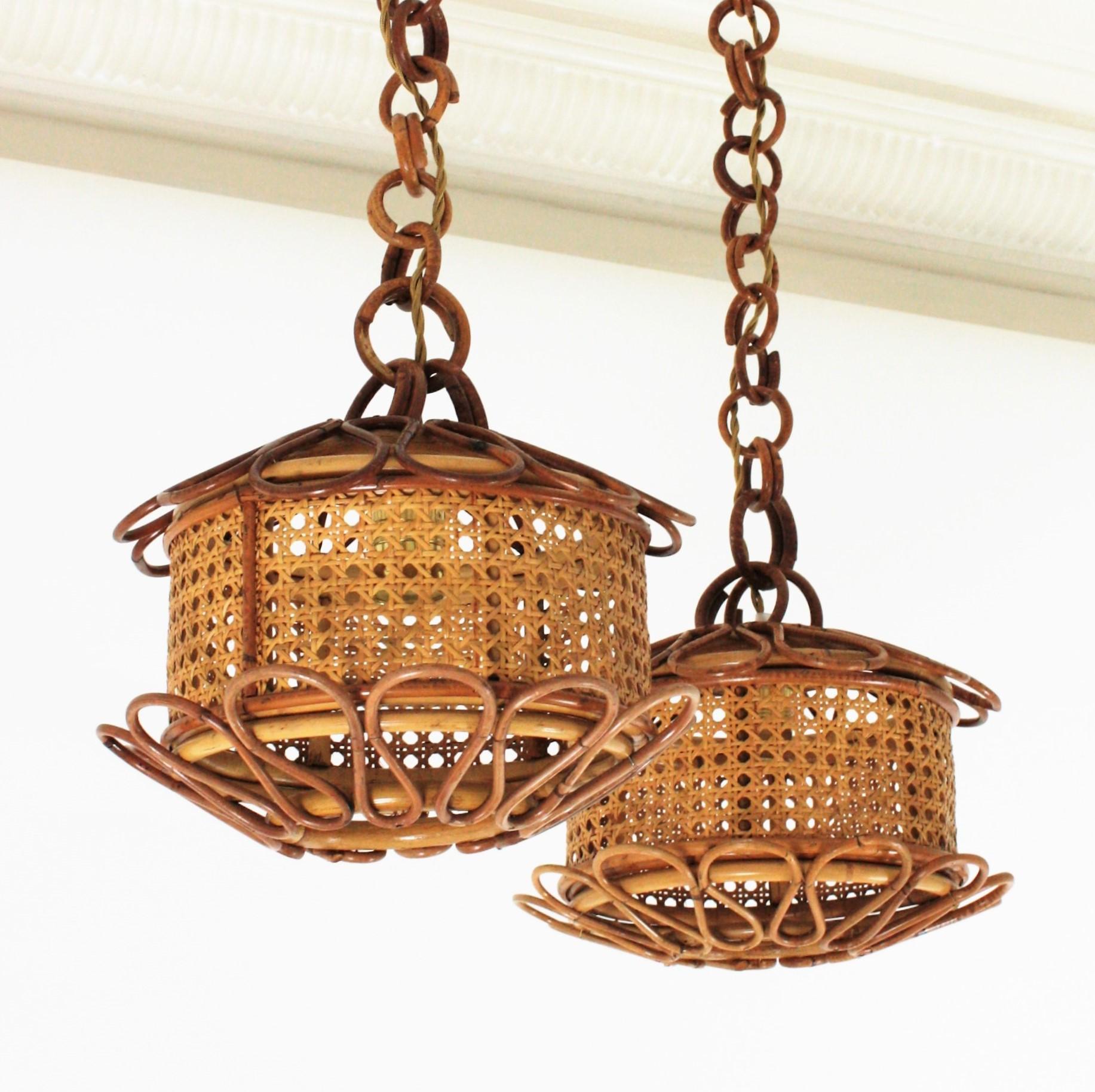 Pair of Mid-Century Modern woven wicker wire and rattan pendant lamps / lanterns, Italy, 1950s.
The woven wicker cylindrical shades of these lamps are accented by handcrafted rattan details as petals at the bottom part and at the top. They hang