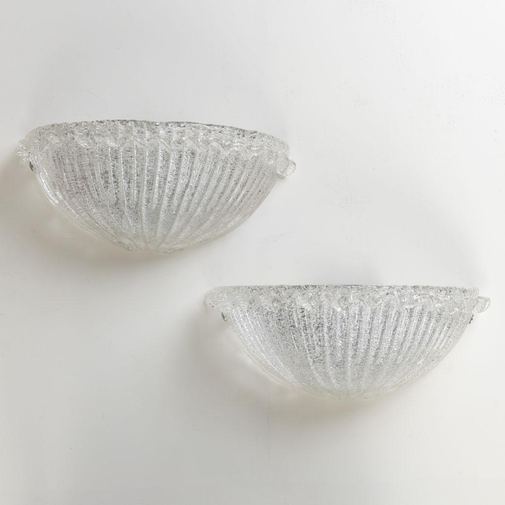 Beautiful pair of Italian Murano glass sconces. Fluted wide shell shape with ribbed detailing in glass and wavy glass detailing along top edge. Chrome screws on sides to attach glass to original chrome backplate. Newly re-wired with single socket in