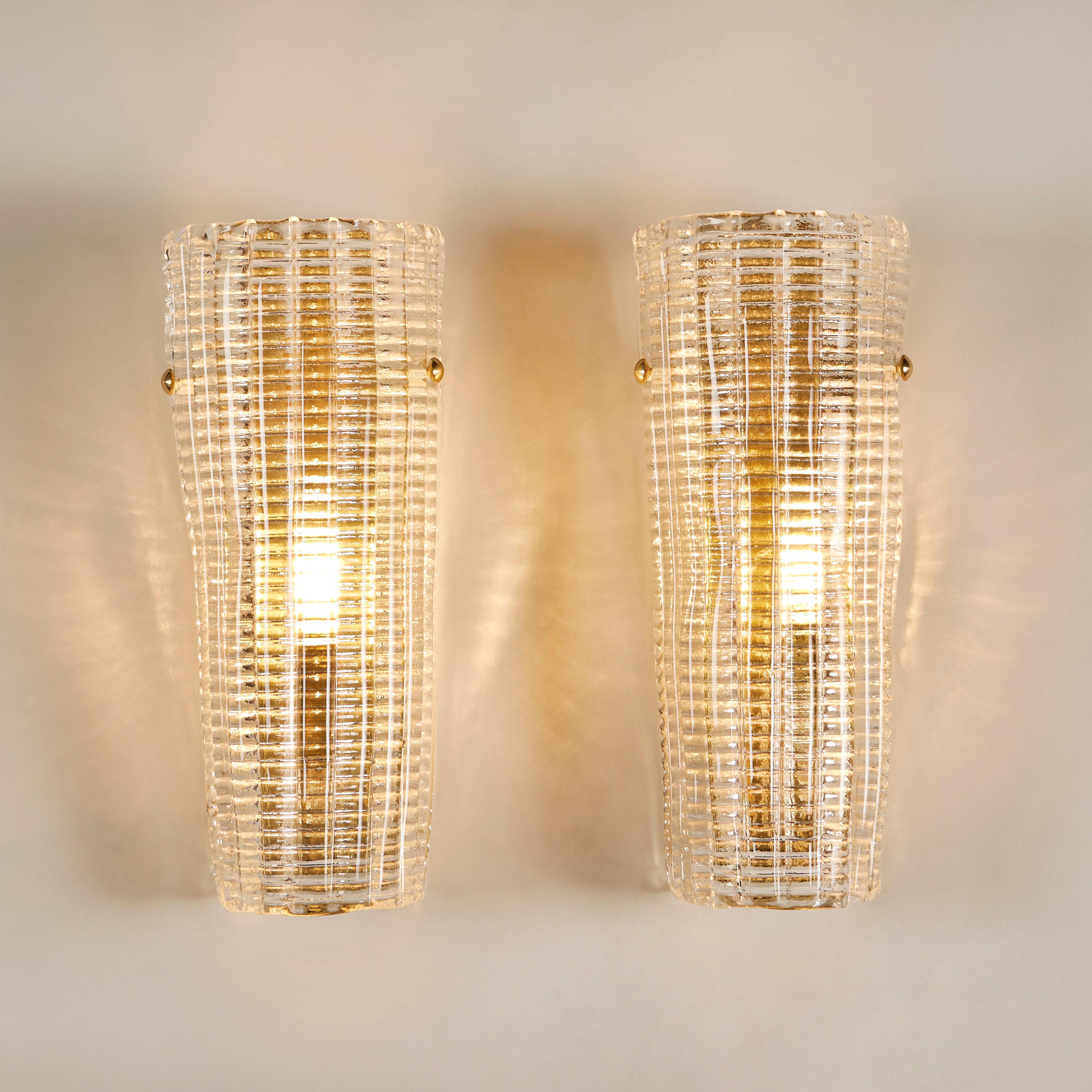 Contemporary pair of substantial tapered Murano wall lights with textured ribbed detail. Full-length brass backplate secure to the glass with decorative filials. The overall effect creates a warm diffused mood light.
 