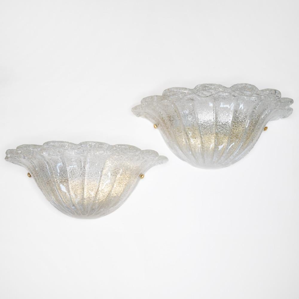 Beautiful pair of Italian Murano glass sconces. Wide shell shape with ribbed detailing in glass and wavy glass detailing along top wedge. Brass screws on sides to attach glass to original brass backplate. Newly re-wired with single socket in each.