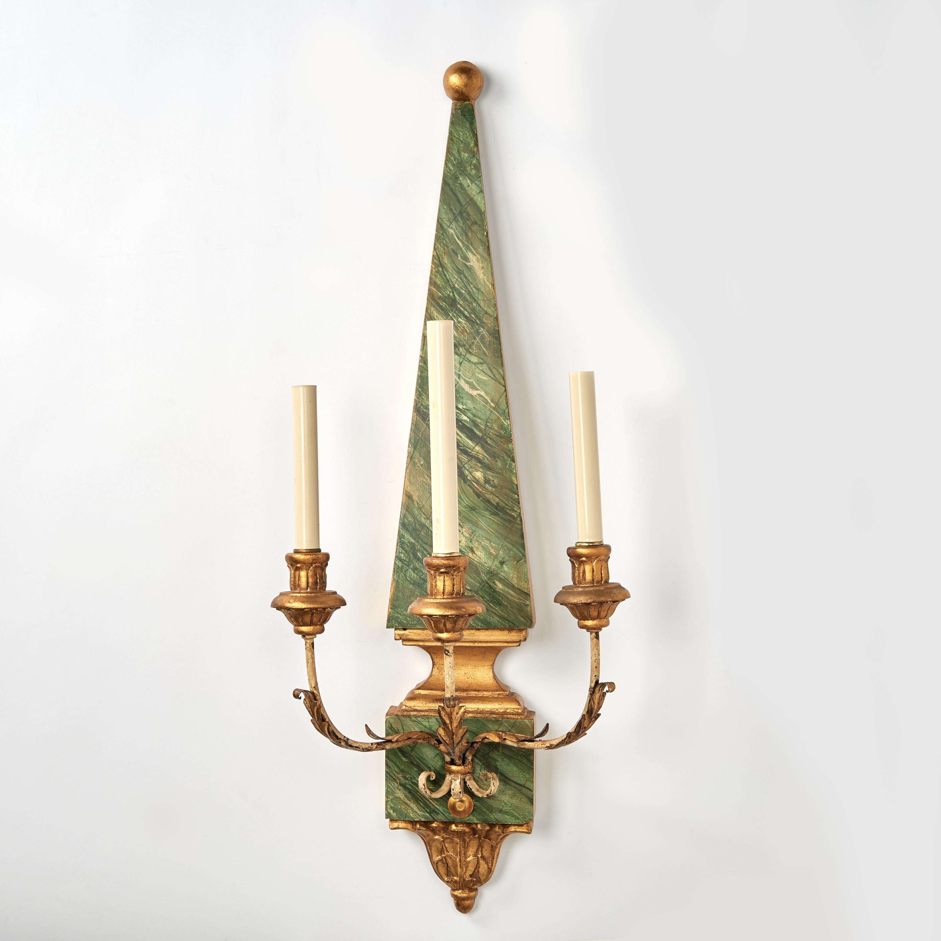 Paire d'appliques murales italiennes anciennes en bois de forme obélisque classique avec une finition en fausse malachite. Trois bras avec des feuilles d'acanthe dorées et des coupes de bougie en bois sur des finales d'acanthe en bois doré.