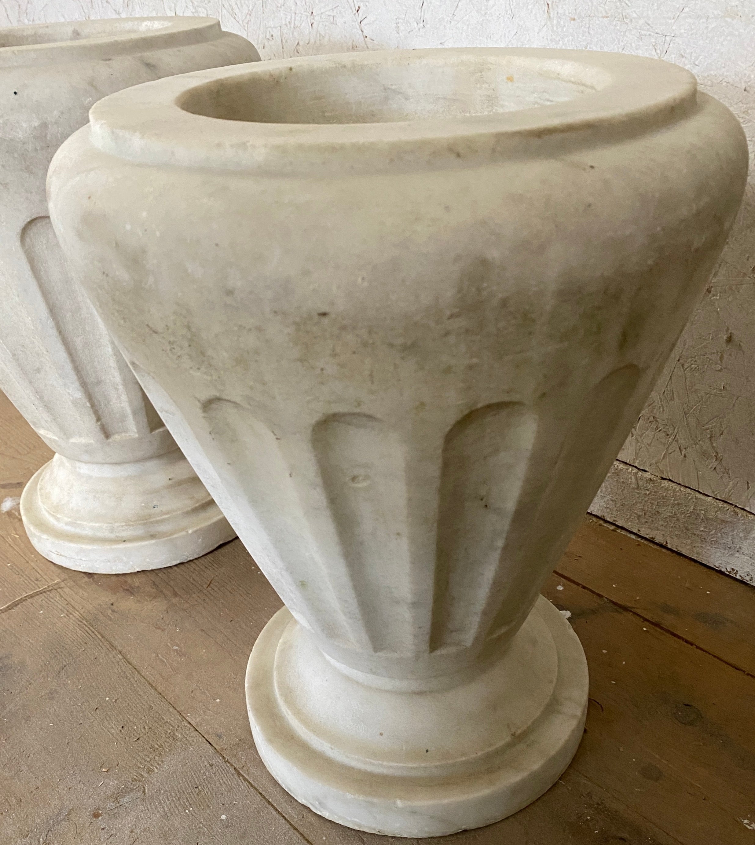 A most attractive pair of Italian Neo-Classical style white Carrara marble urns. Elegant fluted bodies giving it both a clean modern and yet classical look.  Marble shows aged patina giving it character only time is able to provide.  Highly