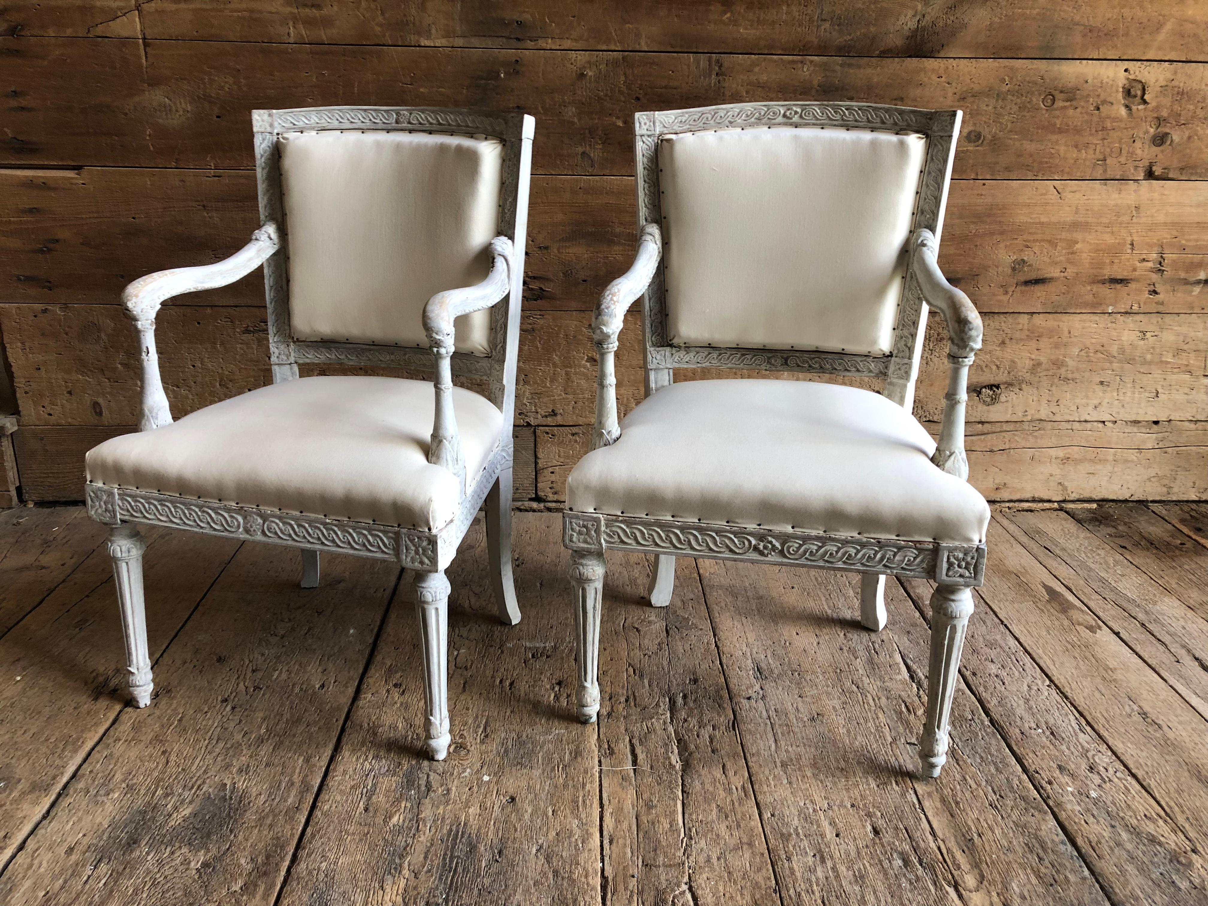 A pair of Italian neoclassic upholstered armchairs in white/grey painted finish, elaborately carved back and seat rails with fluted trumpet-form legs and scrolled arms, circa 1780. Upholstered in cream muslin.