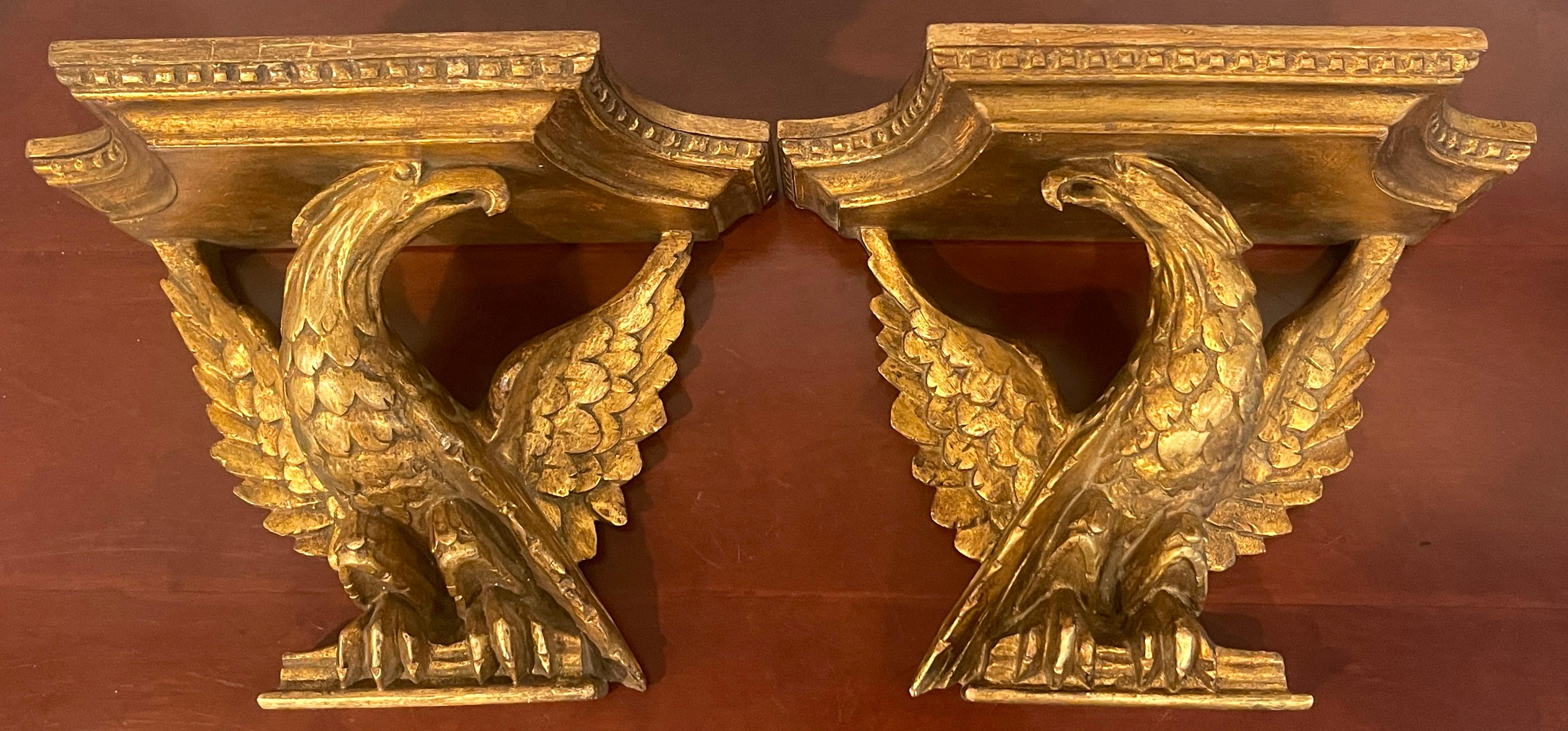 Pair of Italian neoclassic carved giltwood eagle motif wall shelves, each one finely carved of a sitting eagle with outstretched wings. One facing right, the other facing left. With a rectangular tops measuring 11