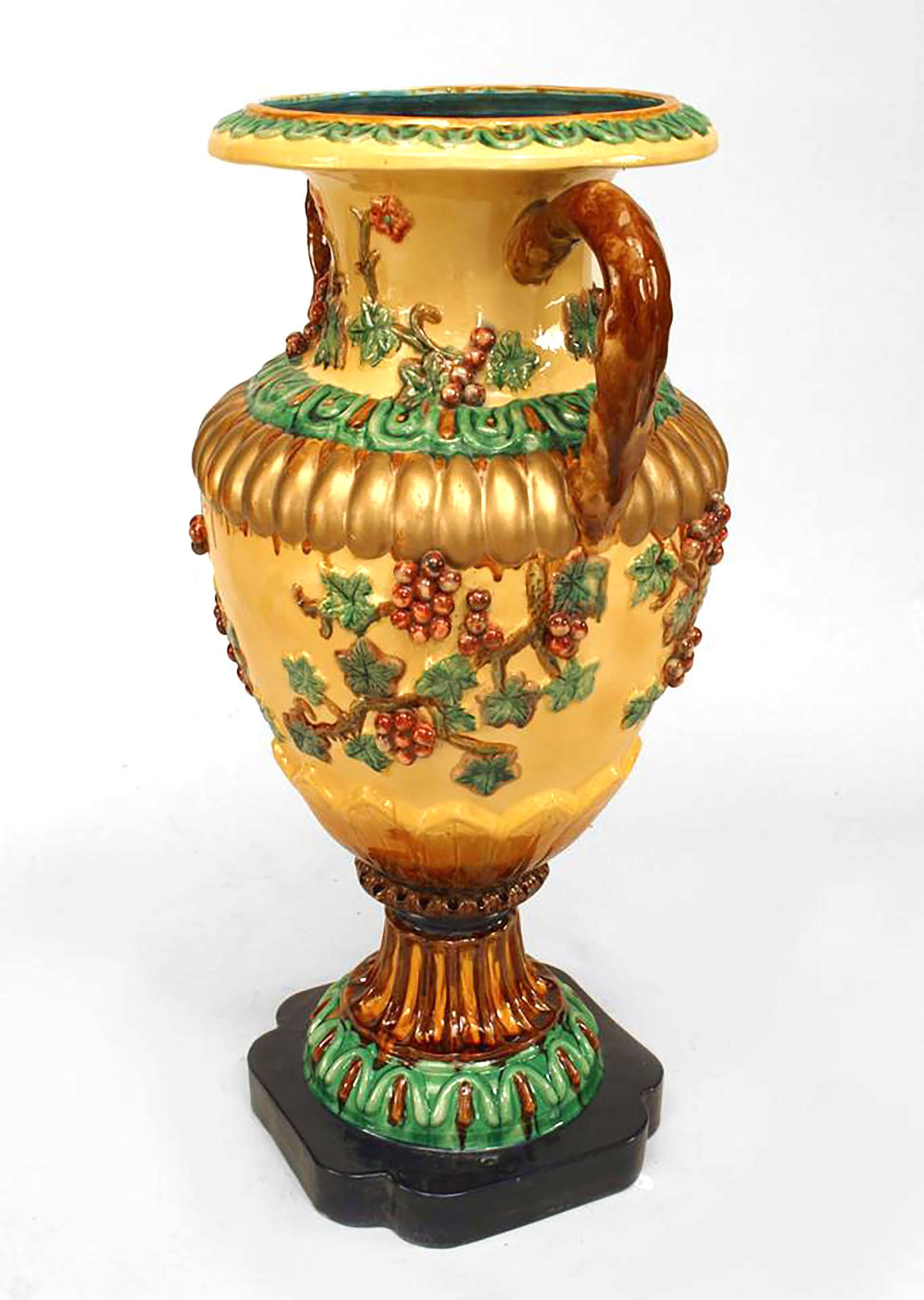 Paire de vases de sol en porcelaine émaillée jaune et verte de style néo-classique italien (19/20e siècle) de style Majolica. Avec de grandes poignées brunes et un décor floral avec des raisins en relief sur une base carrée bleue. (Prix de la