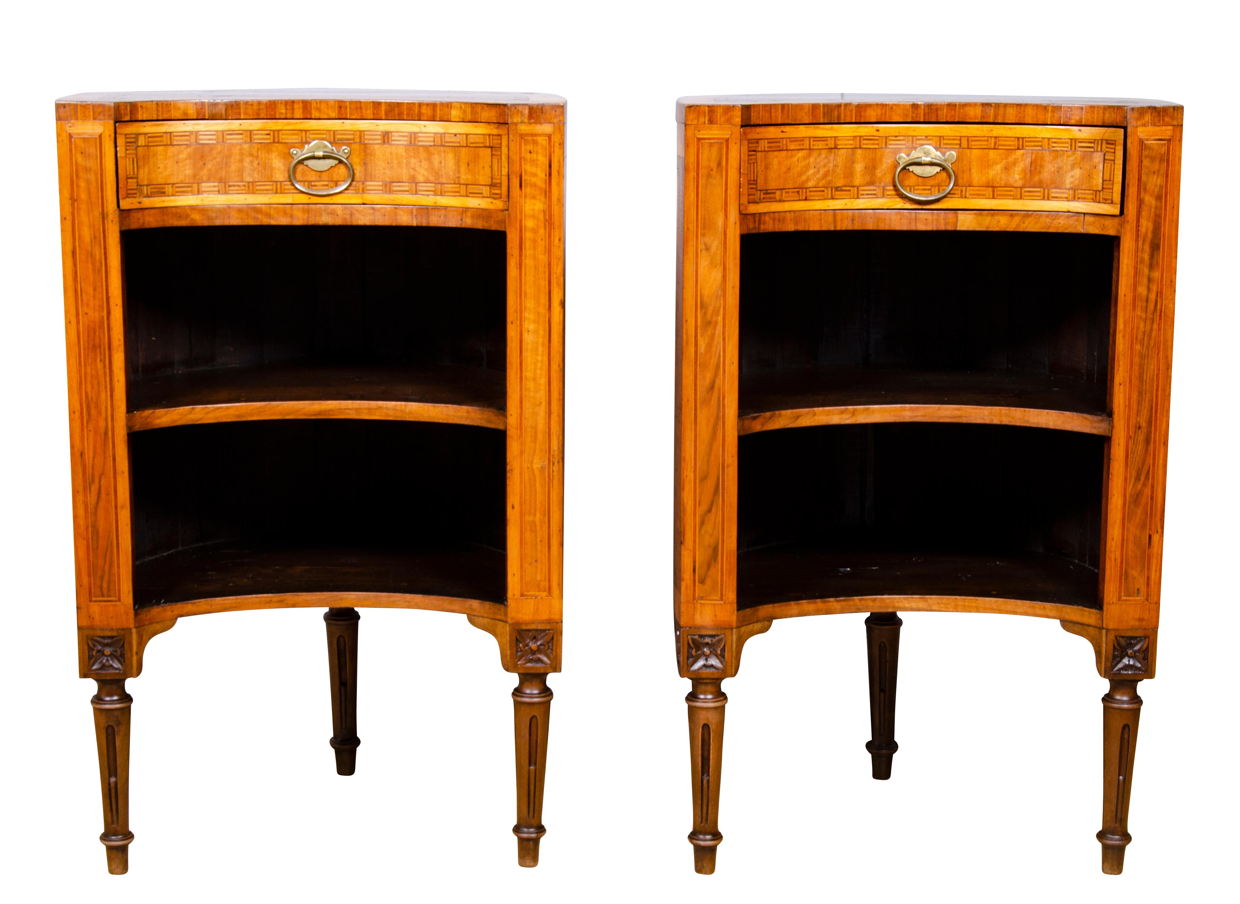 With oval tops and concave front and rounded finished backs over a conforming drawer over an open compartment with a shelf raised on three circular tapered fluted legs headed by paterae.