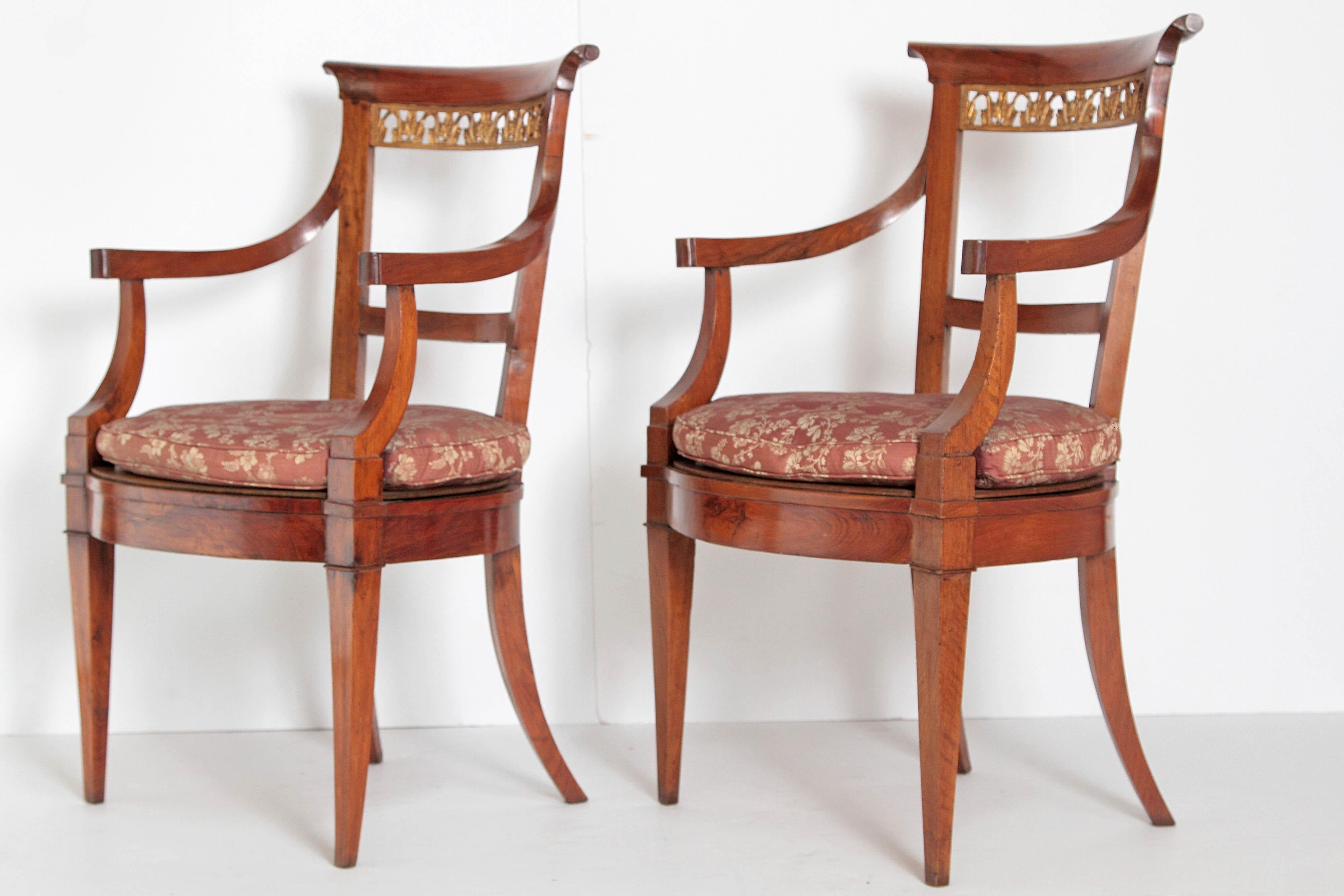 An elegant pair of neoclassical Italian walnut armchairs. A nicely carved crest rail with a gilded trellis. Loose cushion on seat and saber form rear legs with square taper front legs, early 19th century, circa 1810, Italy.