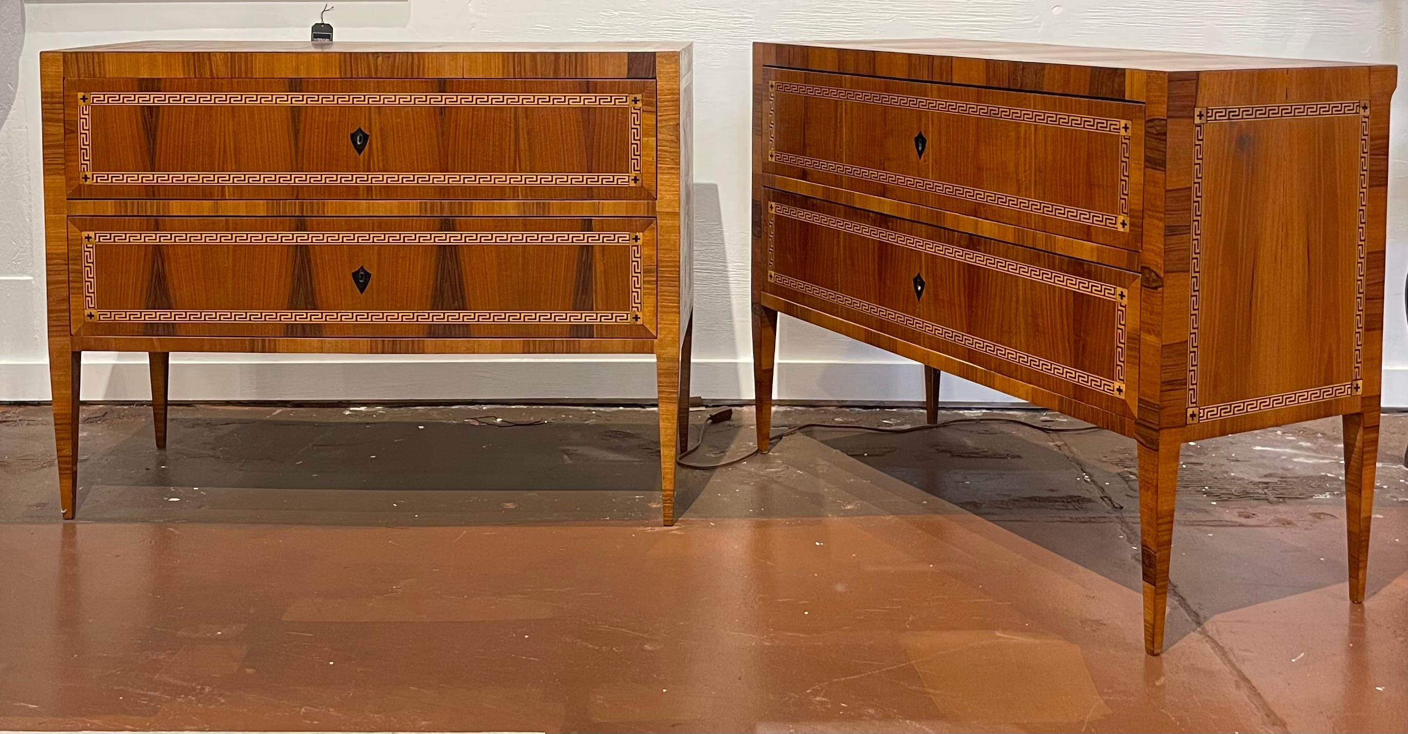 Fine quality pair of Italian Neoclassical commodes having exotic wood veneers and decorative greek key inlays. Each streamlined case holds two inlaid drawers with ebonized shield escutcheons. The drawers' interiors are beautifully lined with