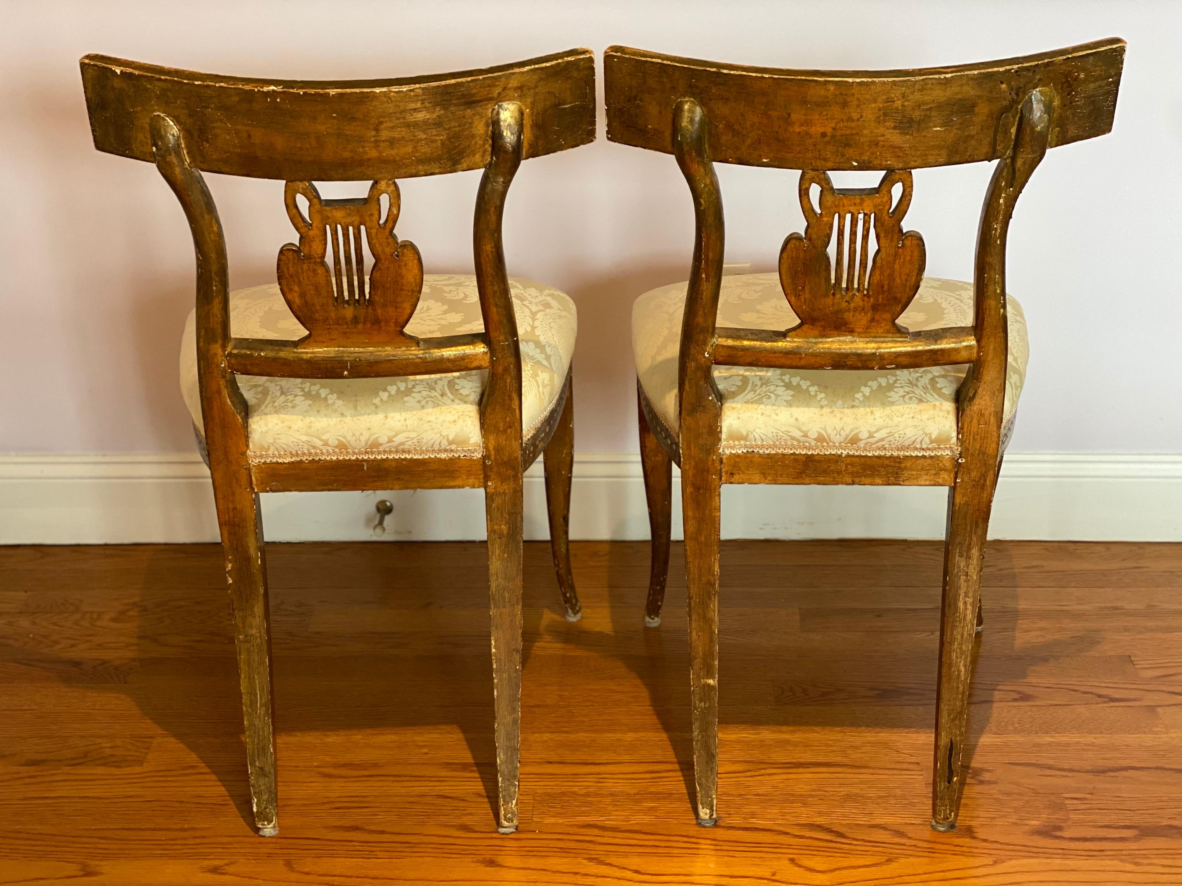 Paire de chaises latérales néoclassiques italiennes en bois doré avec cygnes et lyres, fin C.I.C.
Dos de cygne et de lyre magnifiquement sculptés. Les dos des cadres supérieurs sont incisés et dorés sur un fond peint en ivoire, avec des feuilles