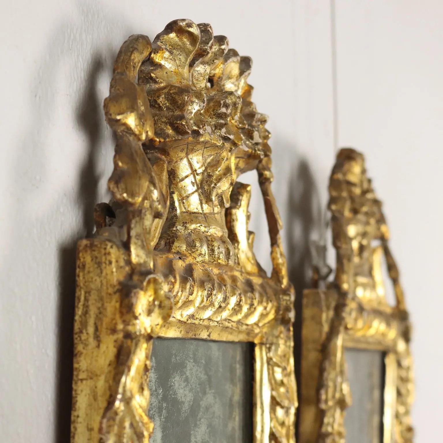 La plaque de miroir rectangulaire est entourée d'une bordure feuillagée, surmontée d'une couronne d'urnes fleuries, entourée d'une tête de fleur et de rinceaux feuillagés. 